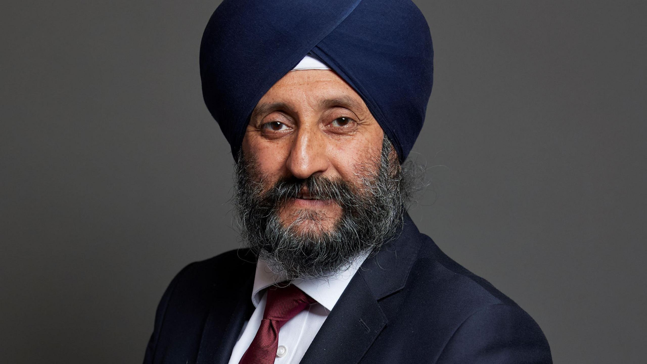 A man wearing a white shirt, reed tie, suit jacket and navy blue turban