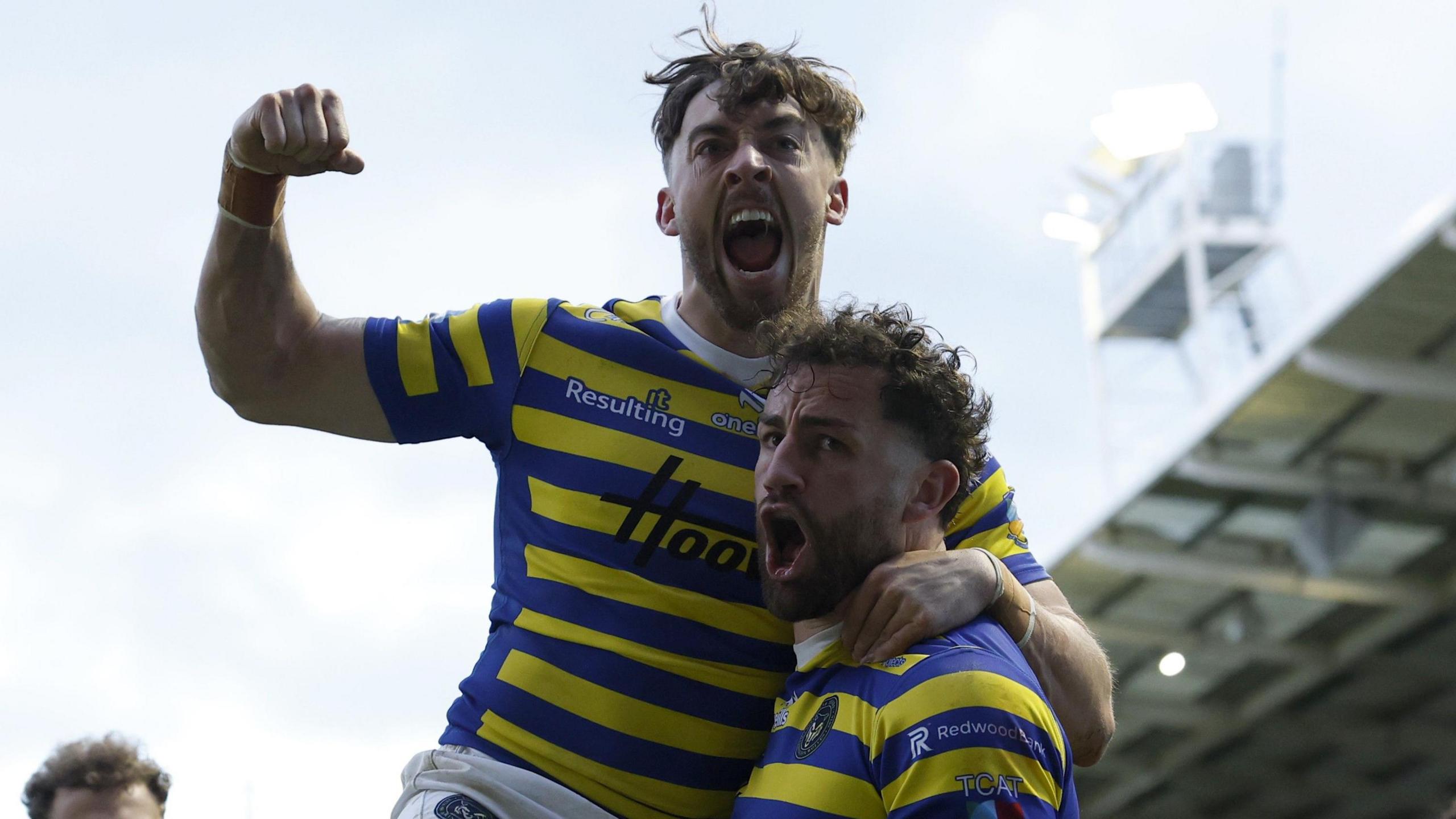 Warrington Wolves' Toby King shouts to celebrate his try while team-mate Matty Ashton leaps on his shoulder and punches the air. Both are wearing Warrington's blue and yellow hoops.