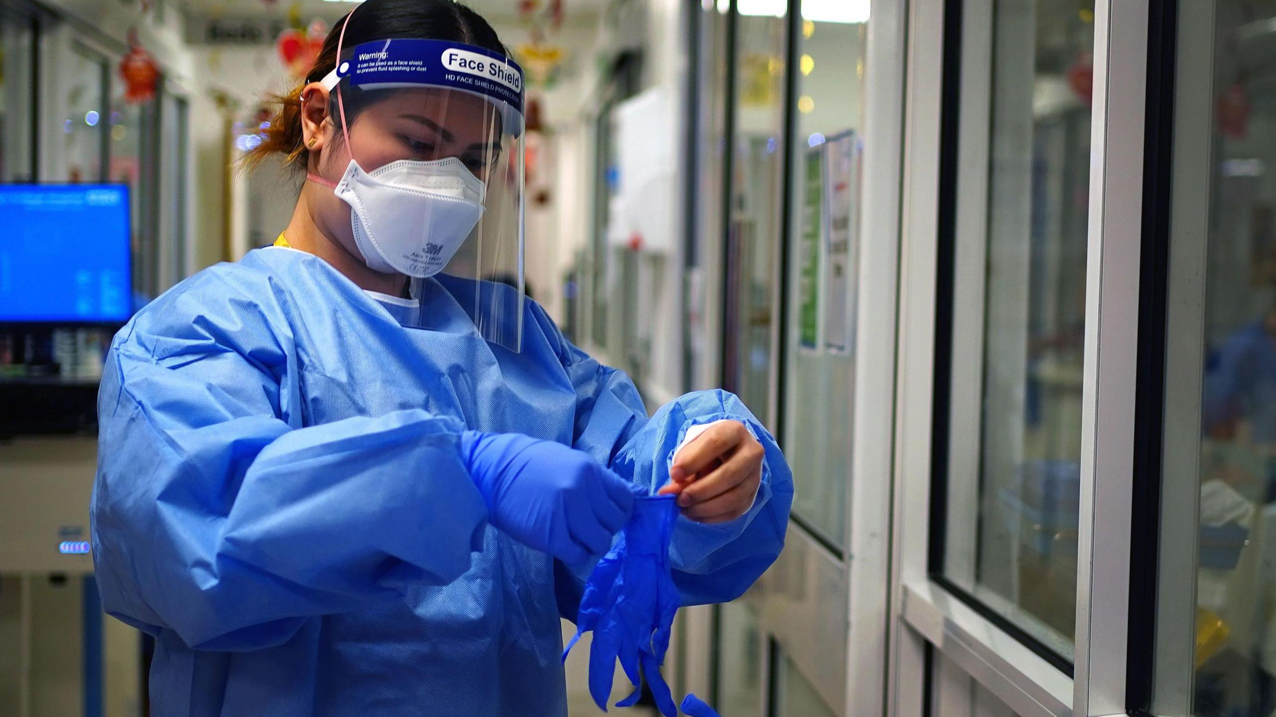 An NHS worker wearing personal protective equipment (PPE) including gloves, gown, mask and a face shield