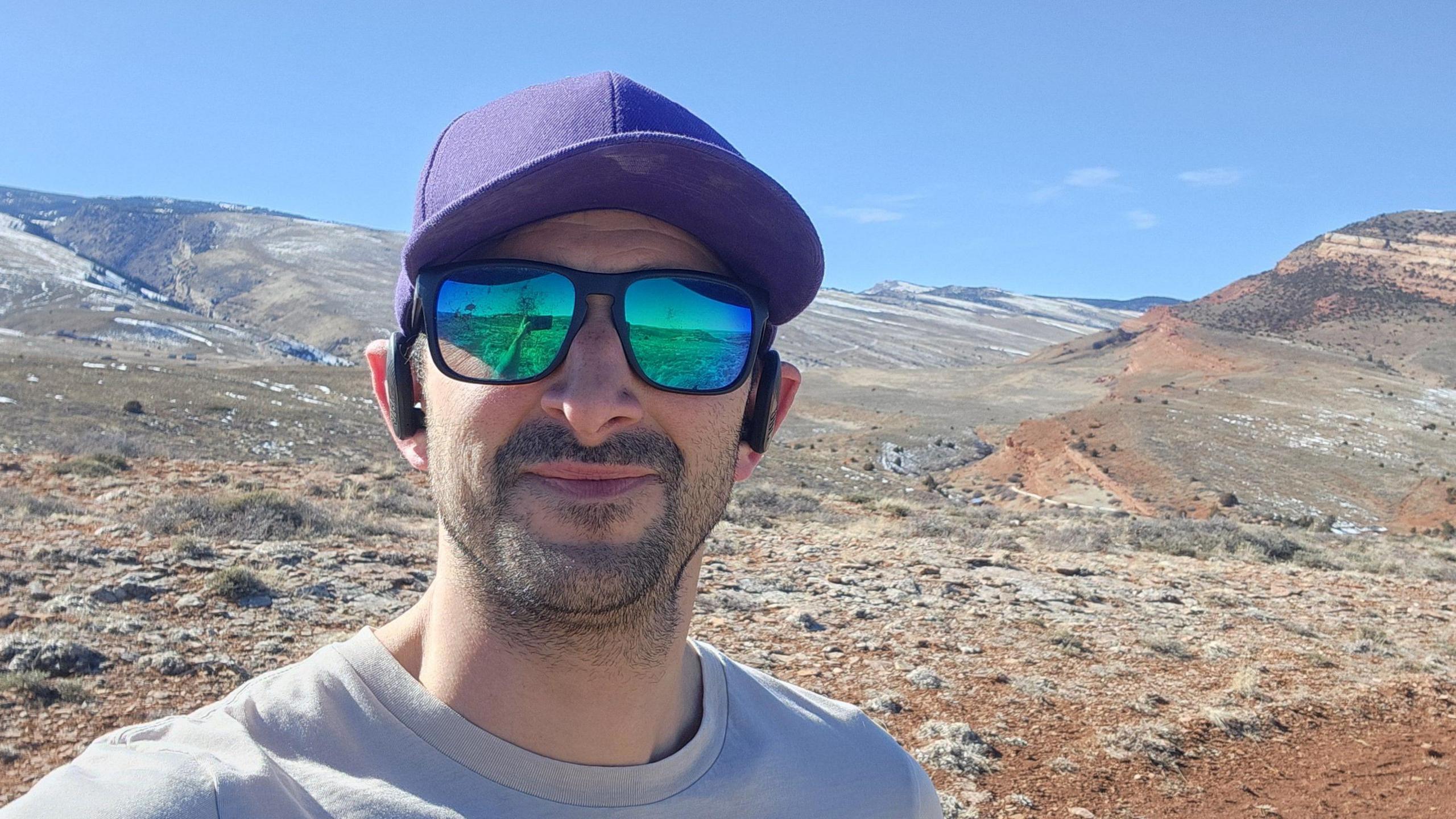 Dave Gold is wearing reflective sunglasses and a purple hat with a mountainous area in the background