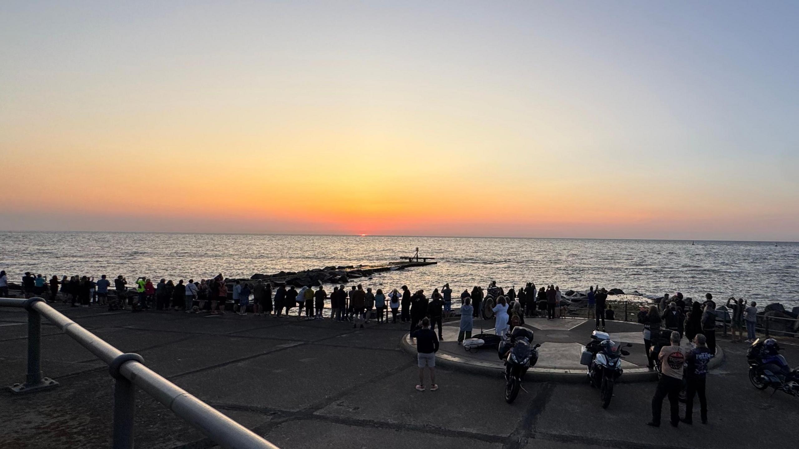 People stood looking out to sea from the UK's most easterly point in Lowestoft, with some motorcyclists in the foreground