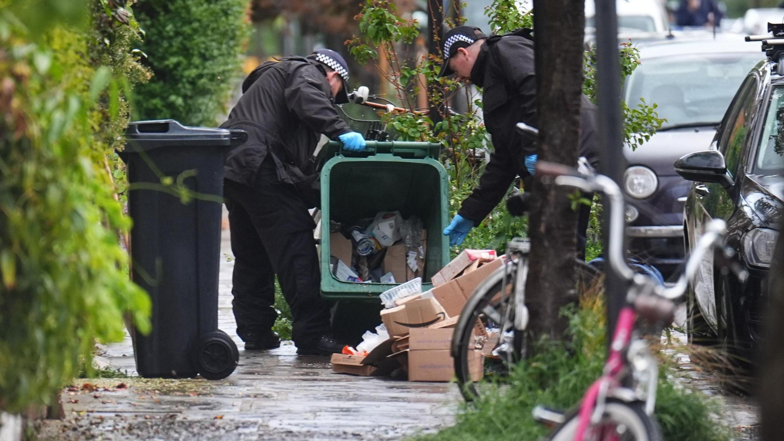 Police officers search a green recycling bin in Kentish Town, north London.