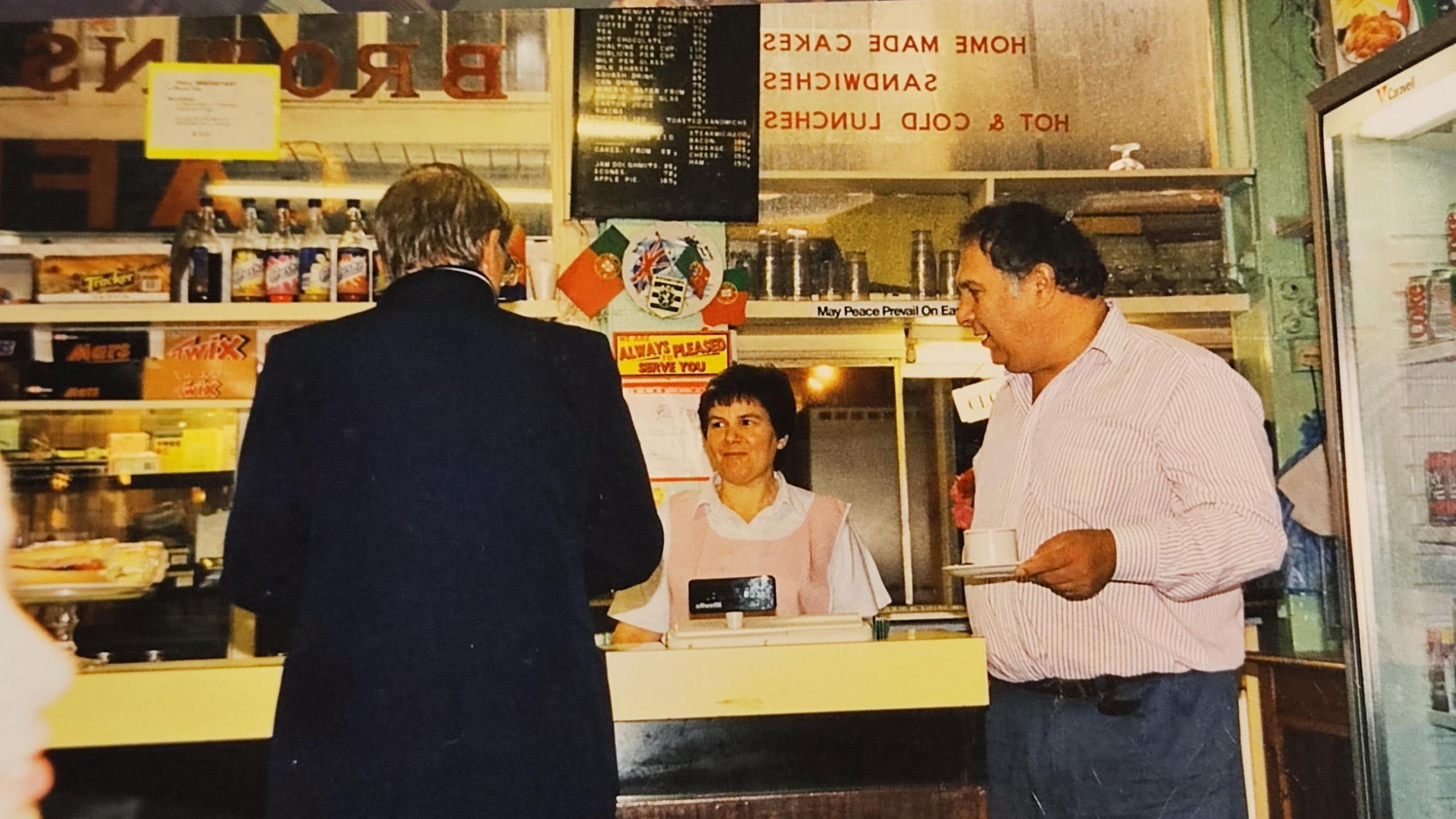 Filomena and Agostinho Freitas behind the counter in Brown's in the 1990s and serving a man in a suit.