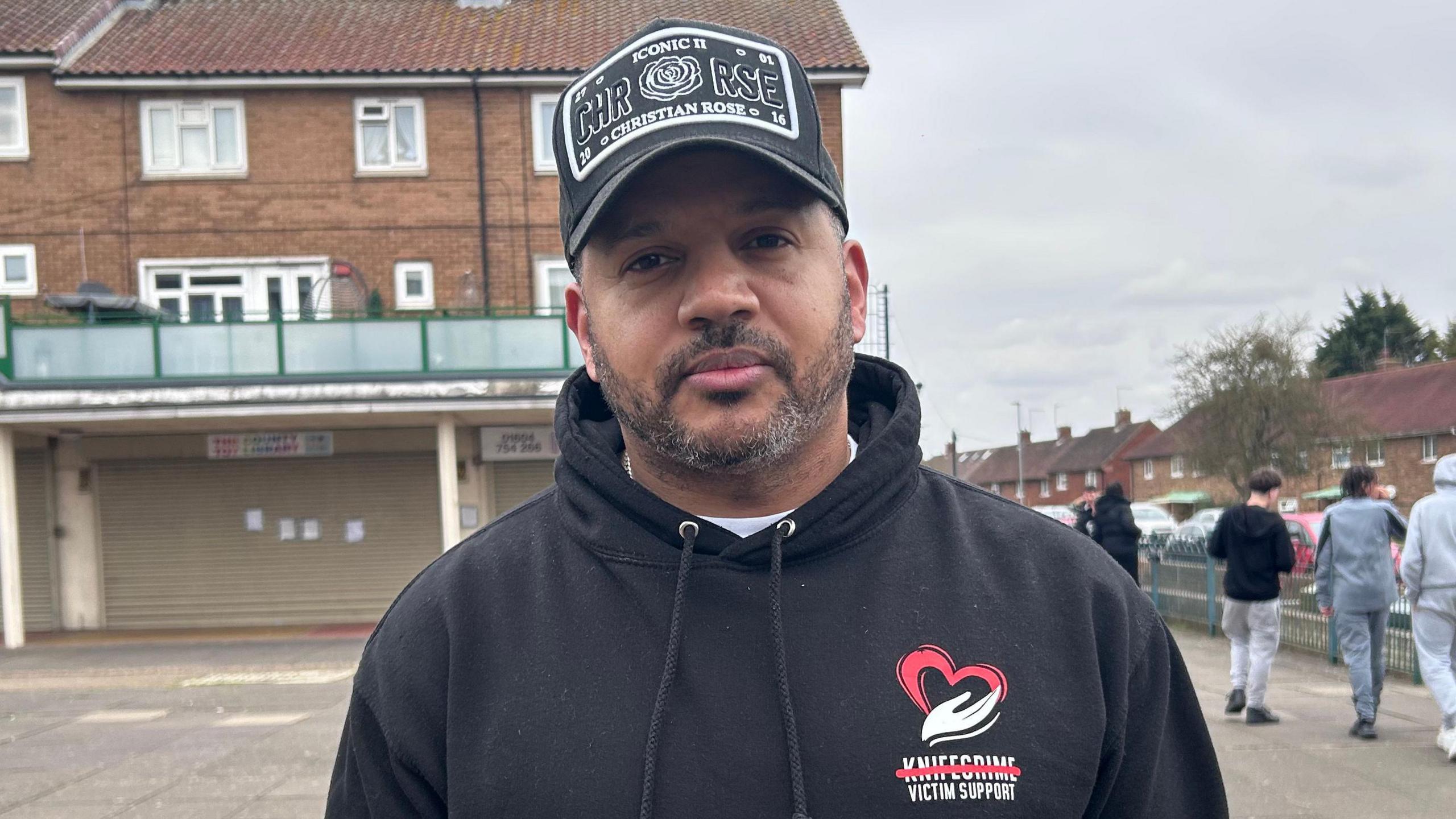 Quinton Green a man standing outside wearing a black hoodie and black baseball cap.