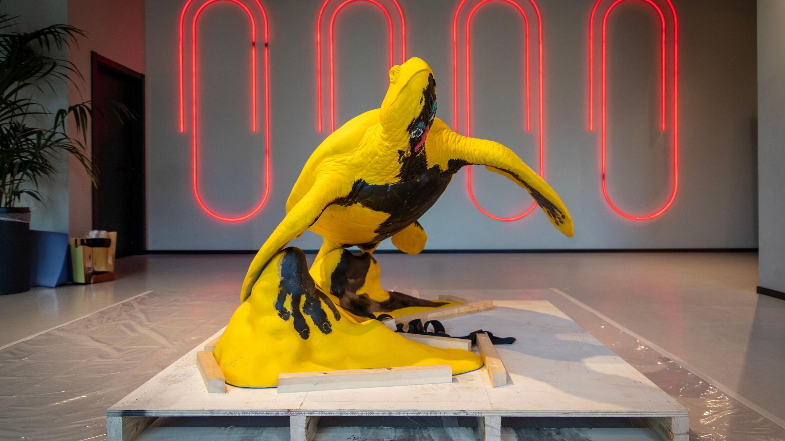A yellow turtle sculpture with a black humanoid figure painted underneath it