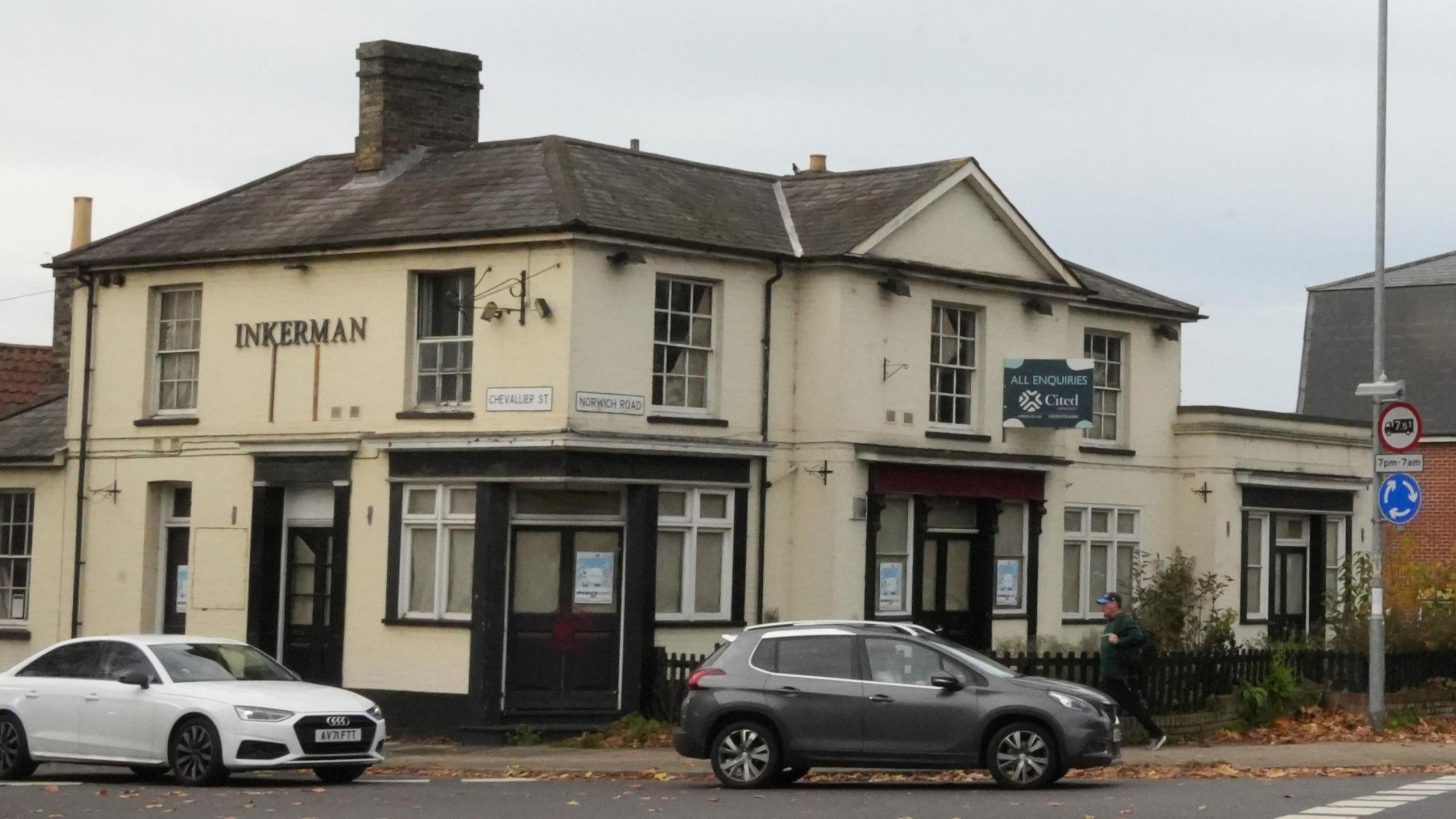 The Inkerman pub building taken from the opposite side of the road. The cream building is closed up with little sign of life. Several cars drive in front of it as they wait to enter a mini roundabout.