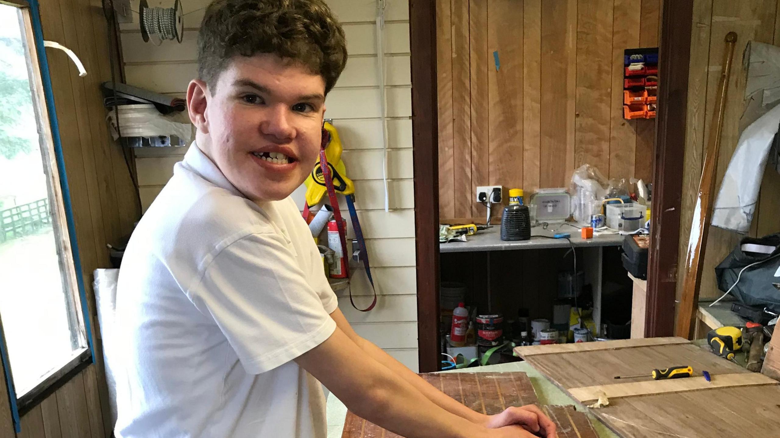 Family photo of Fraser in his dad's workshop holding a tool used to sand down his sailing boat.