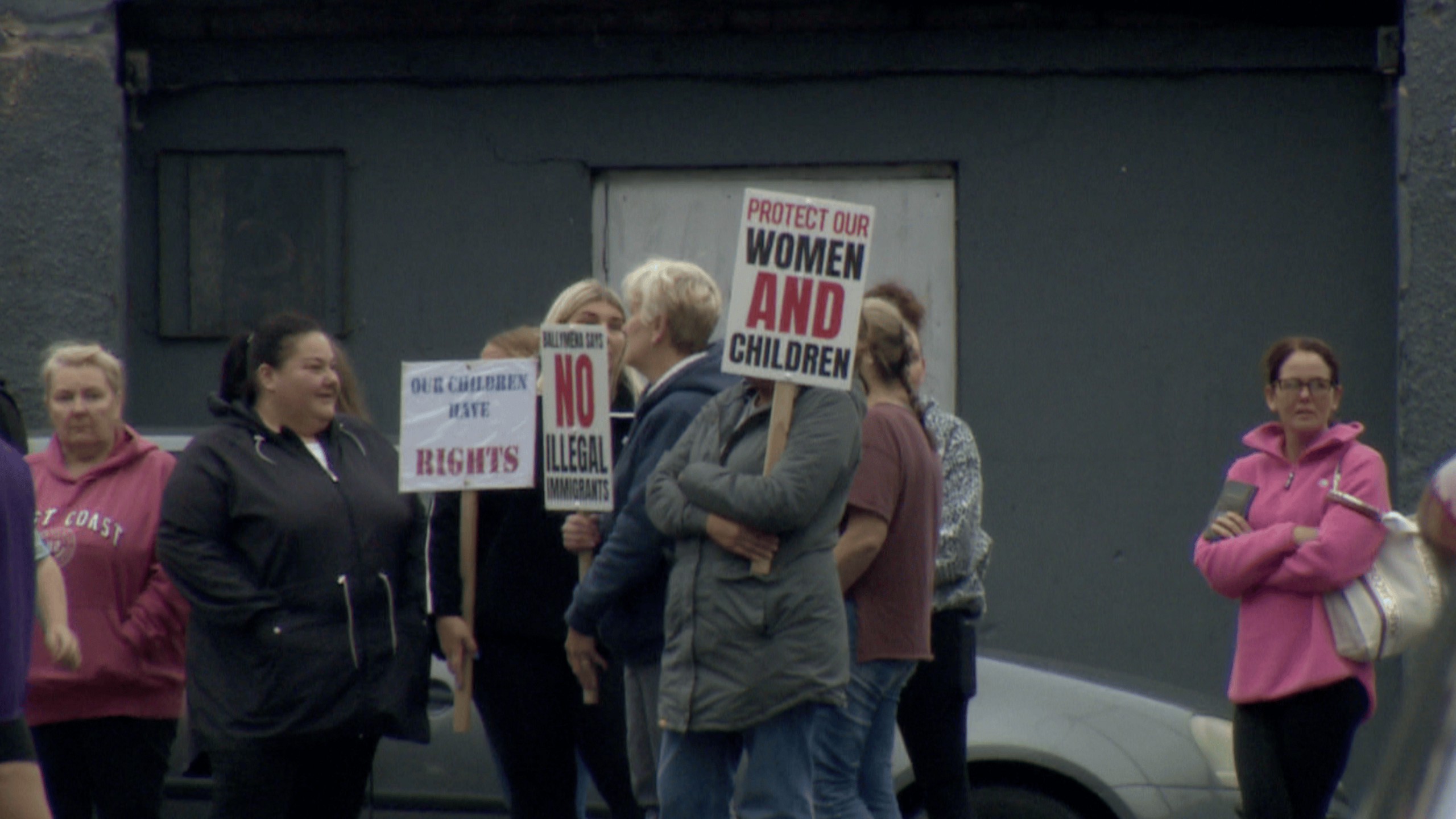 A group of approximately ten women who were among those at a protest in Ballymena. Some are holding signs saying "protect our women and children" and "Ballymena says no illegal immigrants". They are standing on a residential street