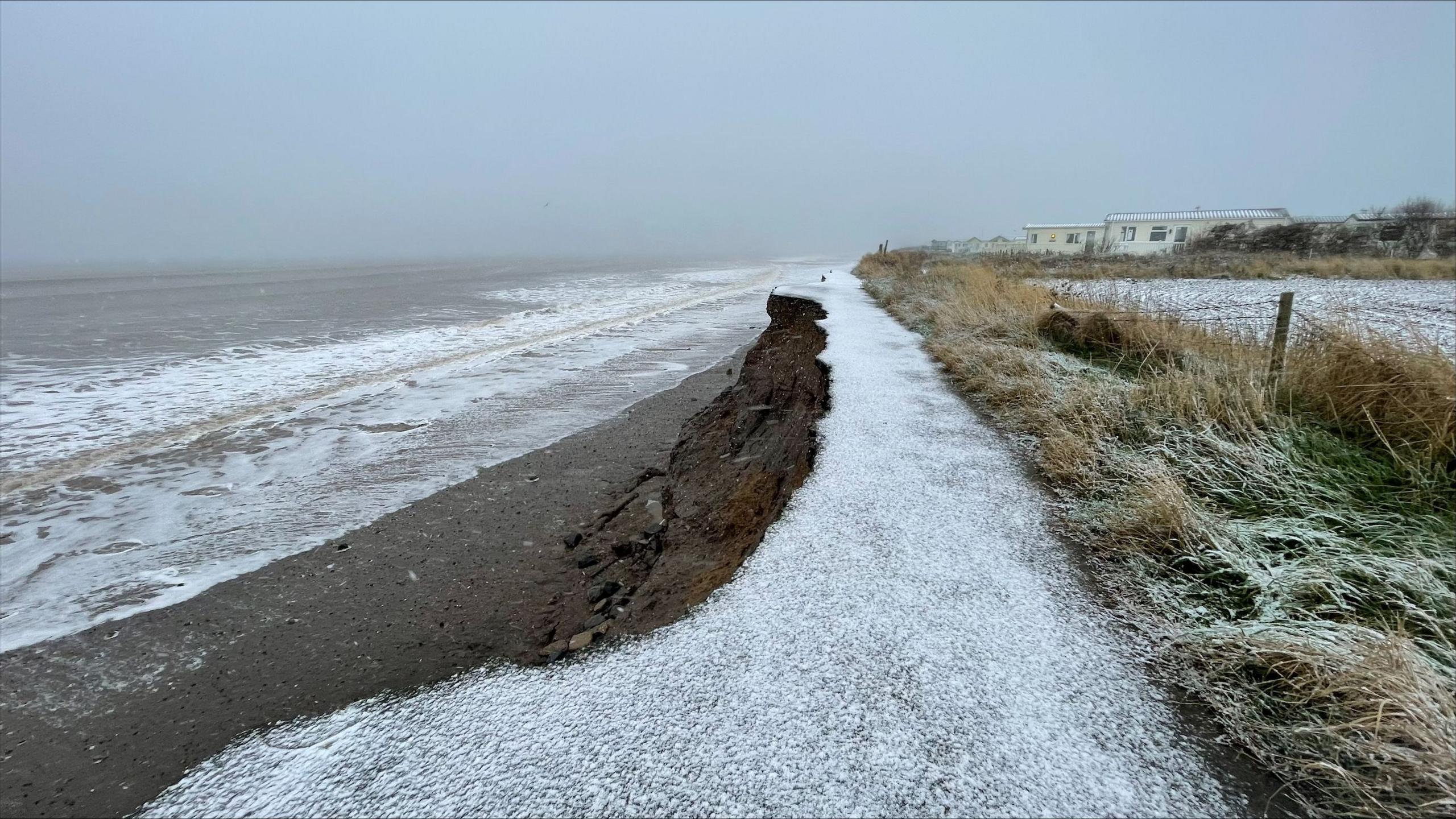 A thin veil of snow on the cliff edge with the sea washing up the clay sand