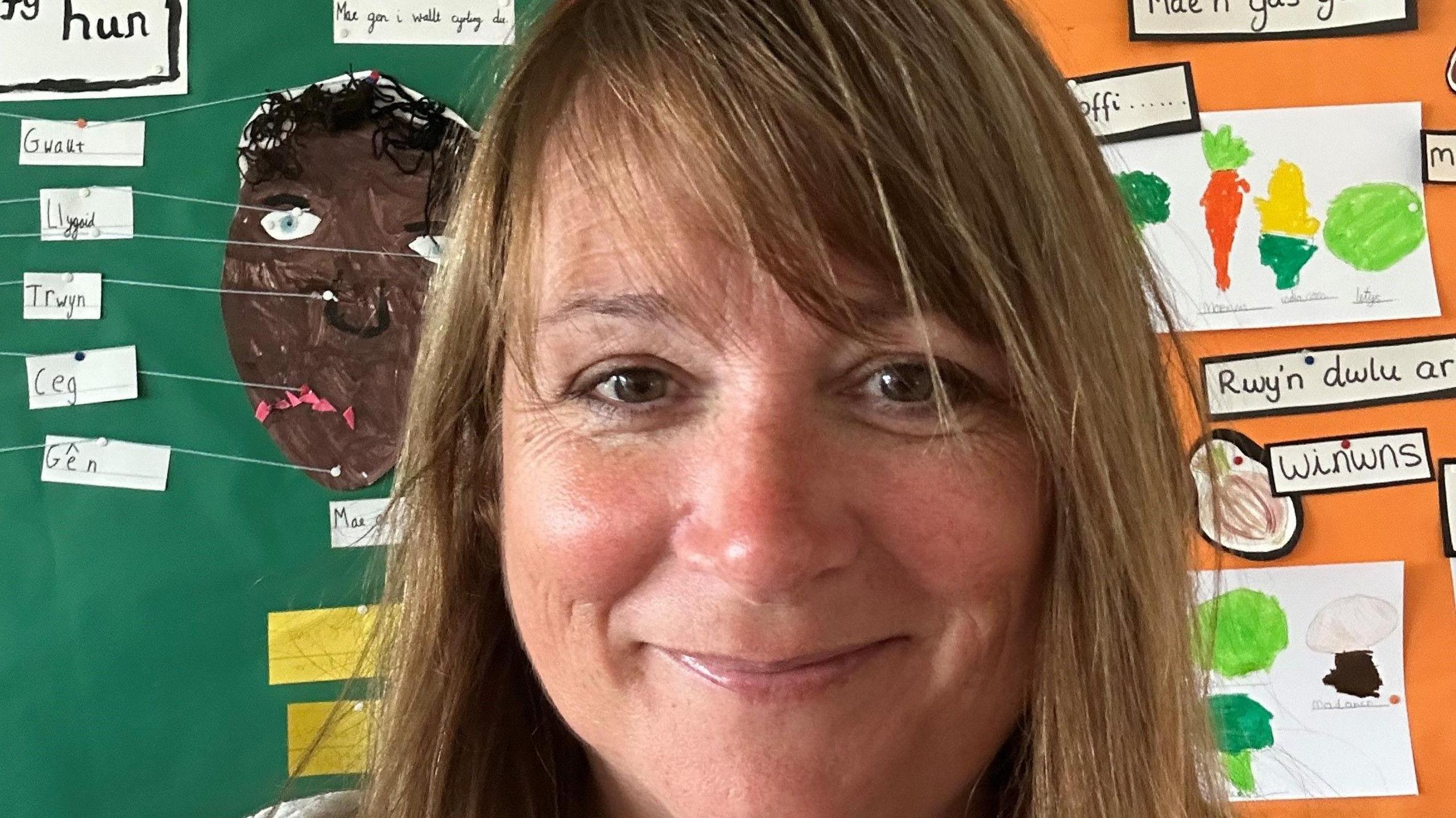 Llun o Rhian James mewn ystafell ddosbarth. Gwaith plant ar y wal y tu ol iddi