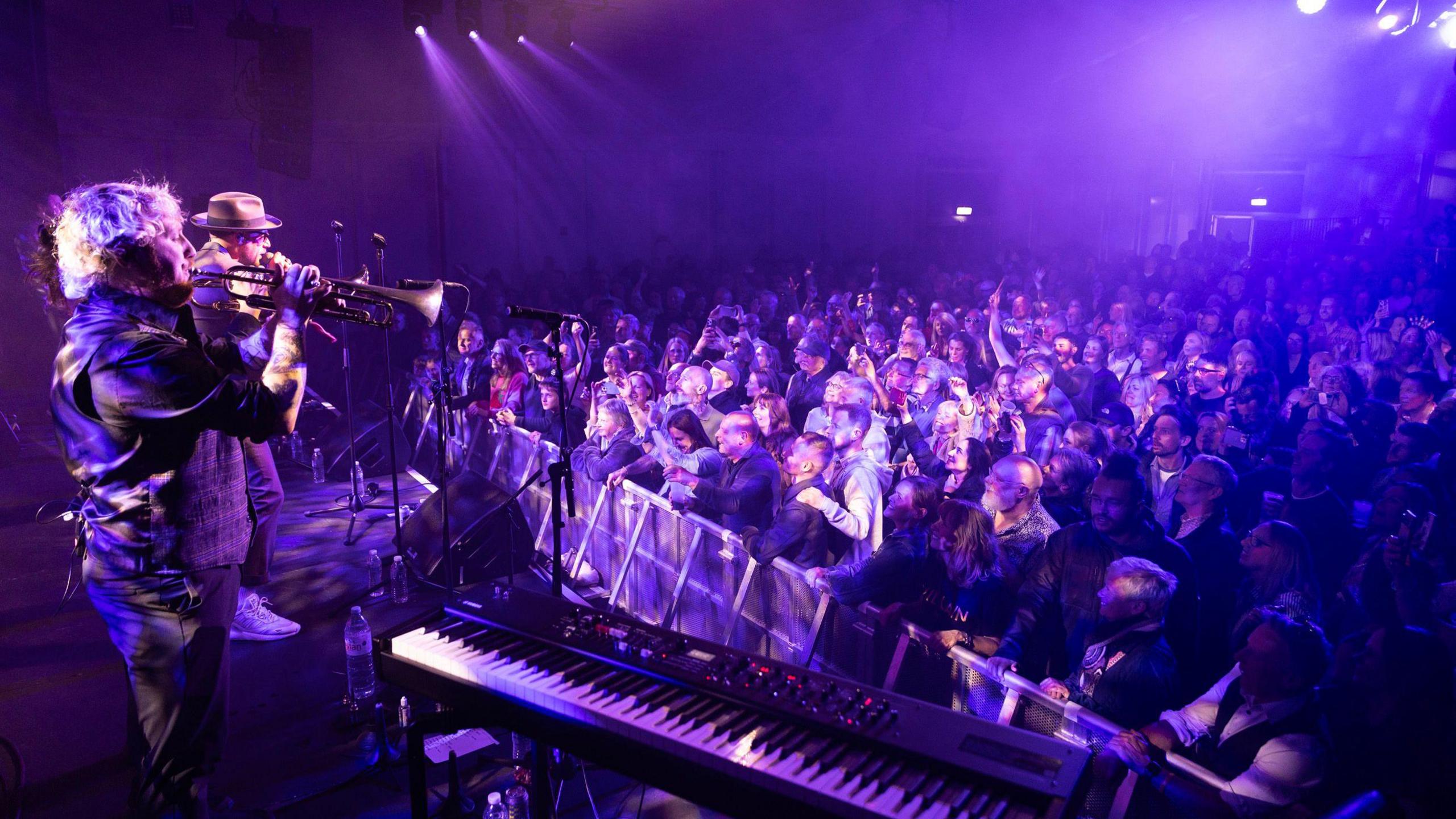A performer at the Cheltenham Jazz Festival sings for the crowd under purple lighting on the main stage at the Cheltenham Jazz Festival.