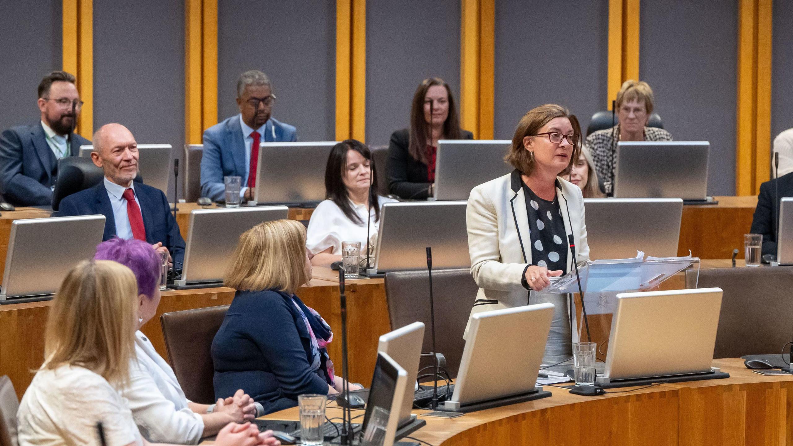 Eluned Morgan ar ei thraed yn siarad yn siambr y Senedd gydag aelodau Llafur yn gwrando arni