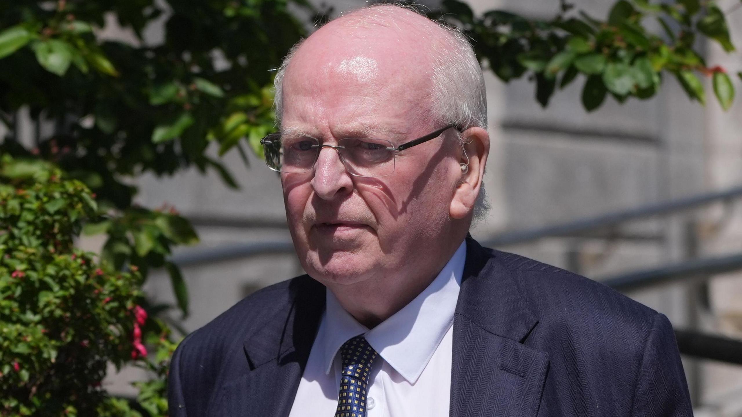 Michael McDowell is pictured leaving the High Court in Dublin. He is an older man and is balding, with some white hairs around the bottom of his head. He has rimless, rectangle glasses and is frowning. He is wearing a dark stripe suit jacket, a white collared shirt and a patterned dark tie.