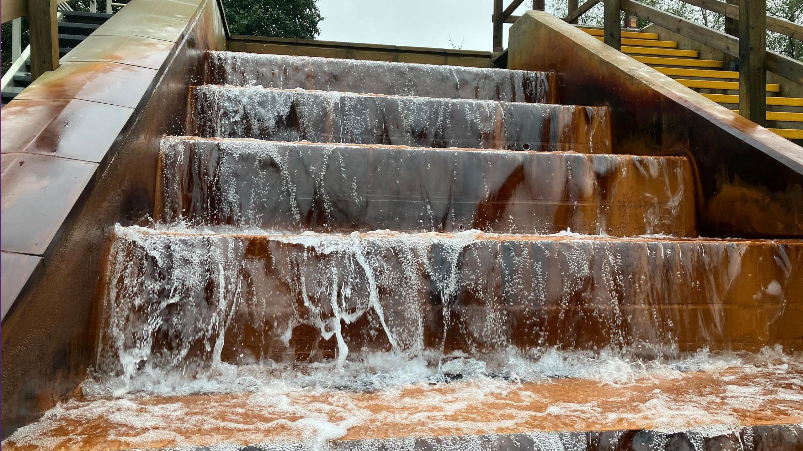 Water which has been pumped from a mine shaft is cascading down four large steps which have turned an ochre colour