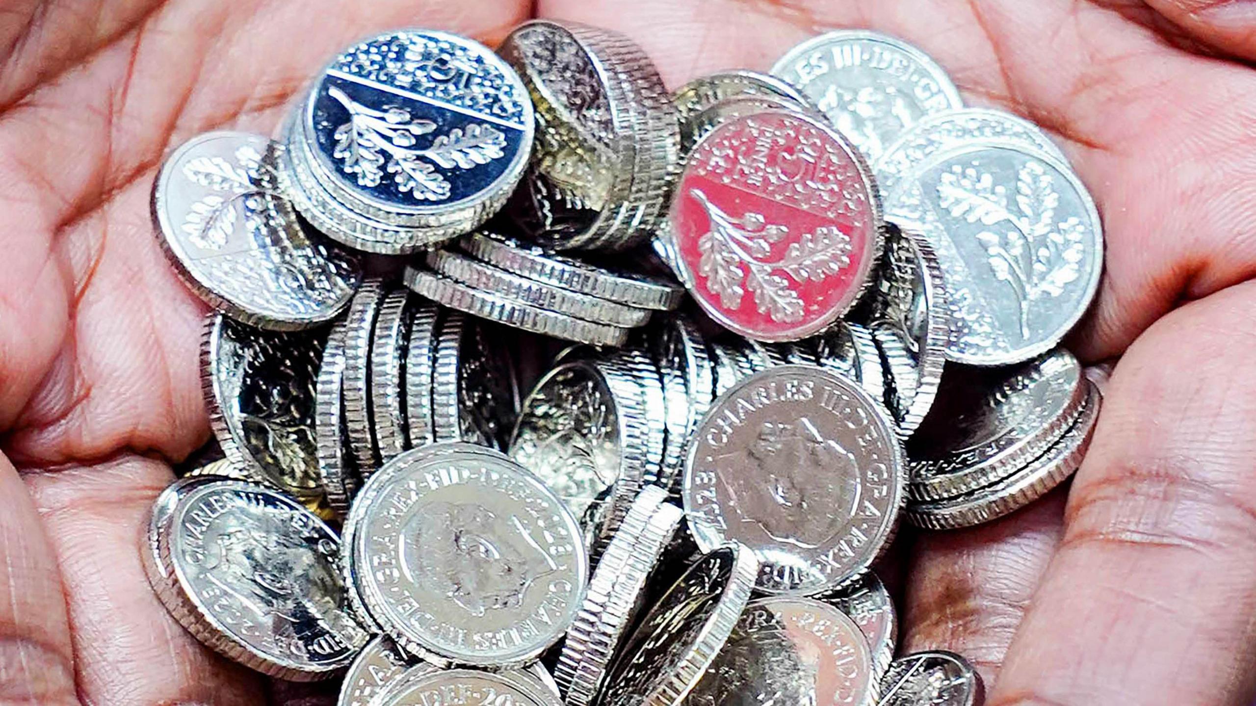 Two hands holding a bunch of the new 5p coins. Some are on the head side which show the Charles III emblem and the other side shows an oak leaf design.