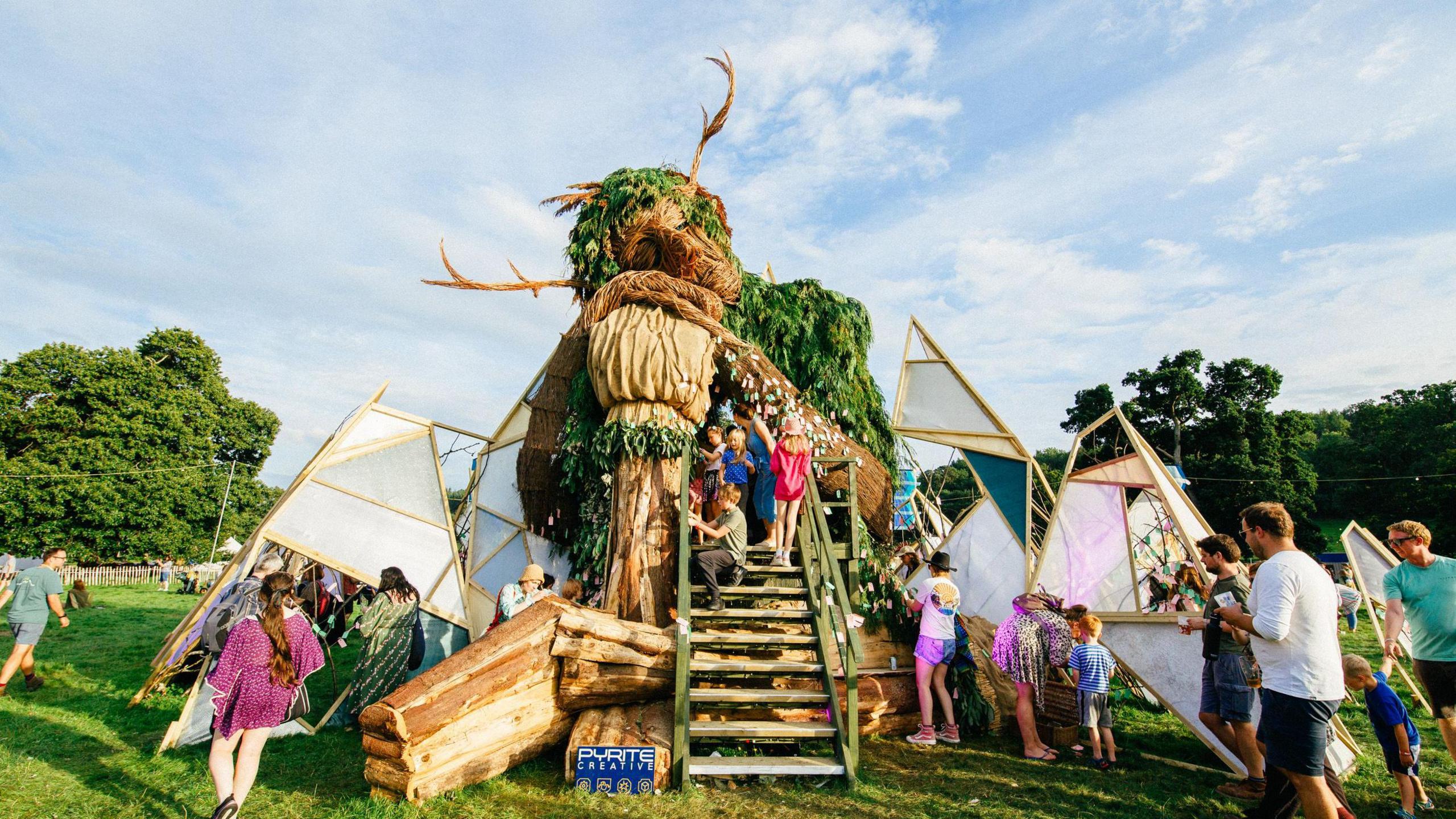 Families and children explore a large sculpture of a Green Man