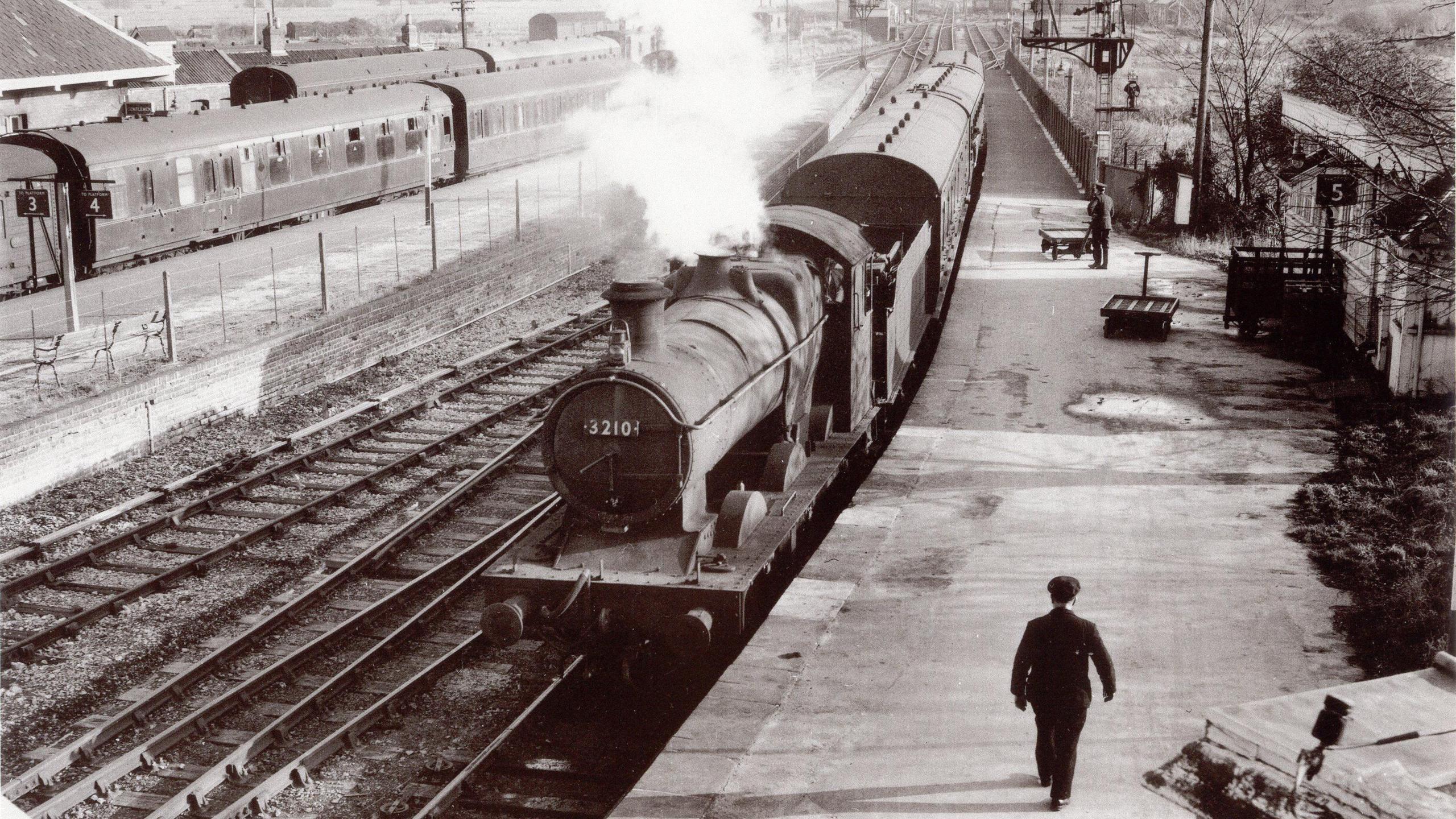 A steam train is coming into Burnham's old station. The photo is black and white.