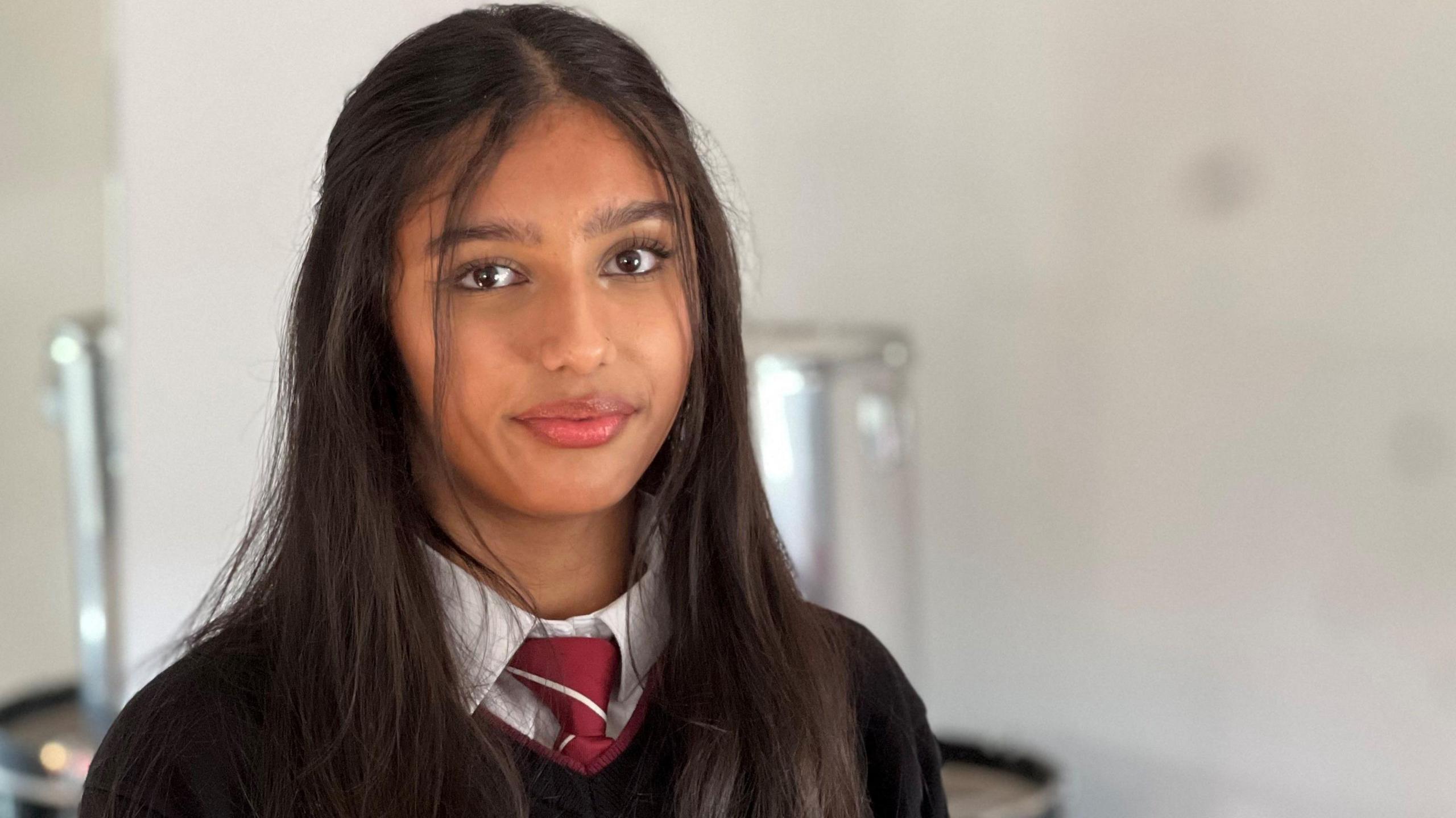 Kia in her school uniform, a black sweater, white shirt and a red tie. She has long black hair 