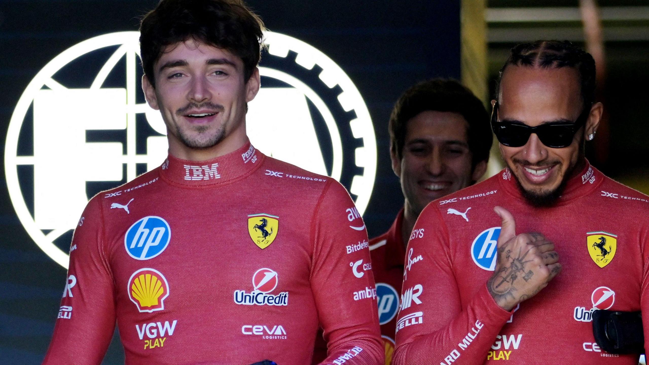 Charles Leclerc and Lewis Hamilton stood next to each and smiling while wearing Ferrari protective clothing