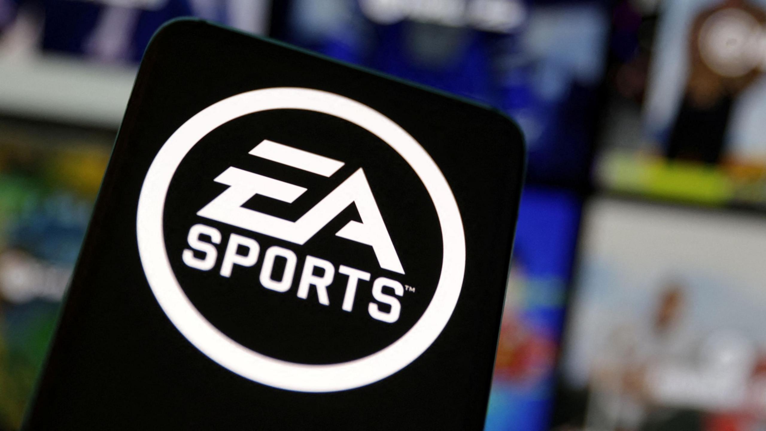 A black sign with the logo of EA Sports in white on it stands in front of a number of blurred screens