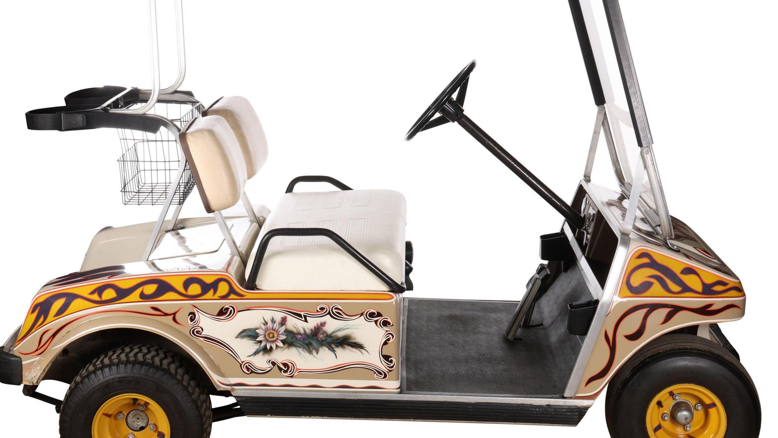 A golf buggy with a yellow, red and navy psychedelic patterned swirls painted on to it, as well as an image of wild flowers