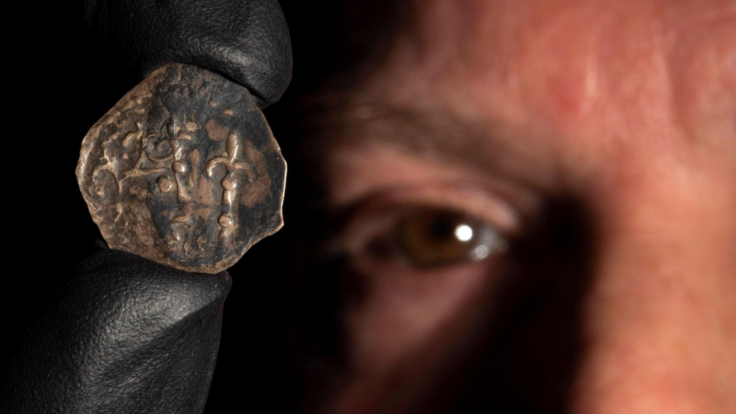 A close up of a bronze coin being held up by a man whose eye is visible in the background