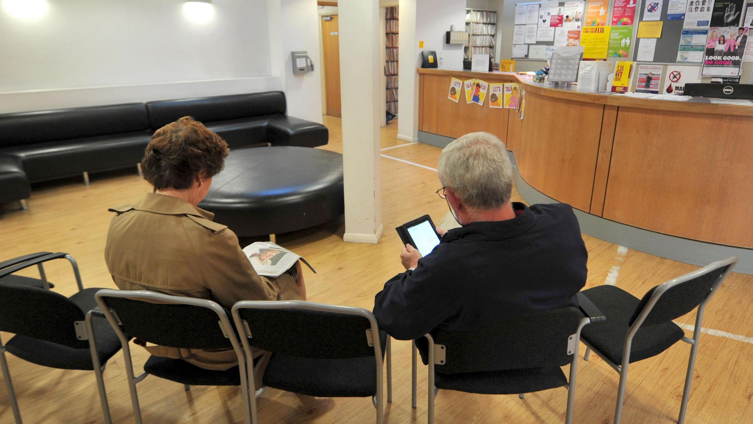 A picture of a GP waiting room with two patients seen from the back