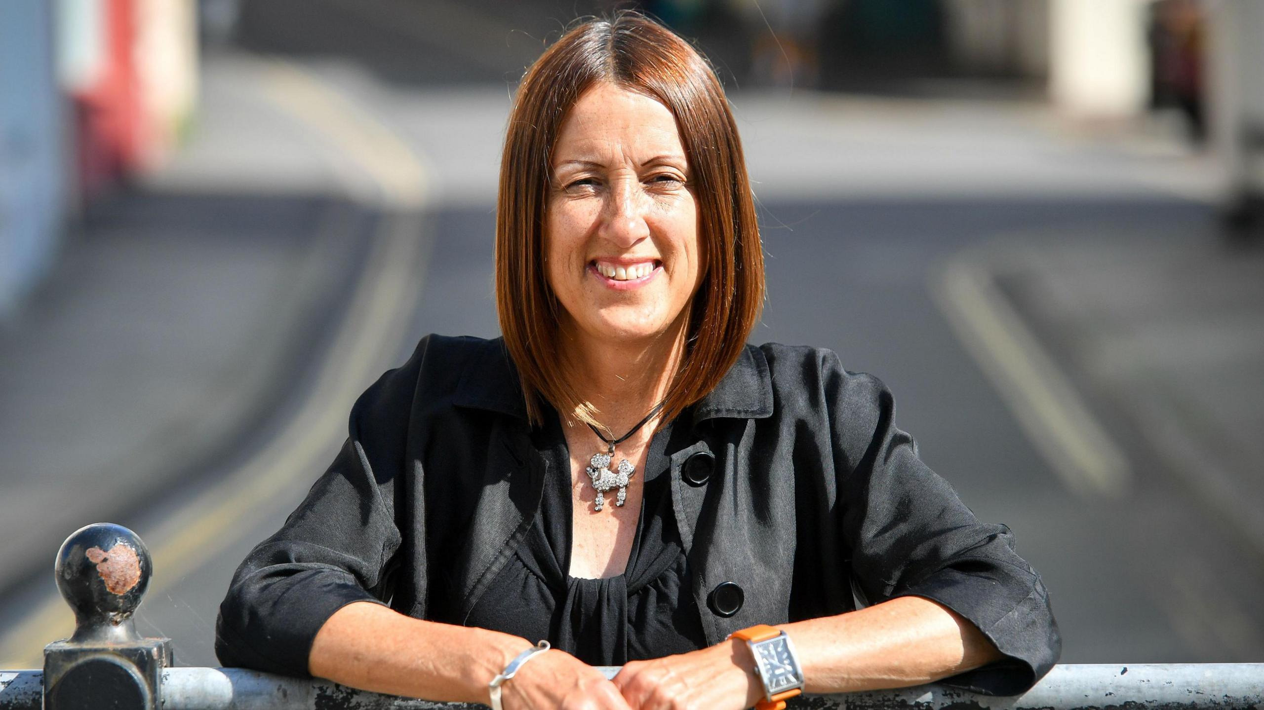 Jane Dodds stood holding a railing at a roadside, looking into the camera.