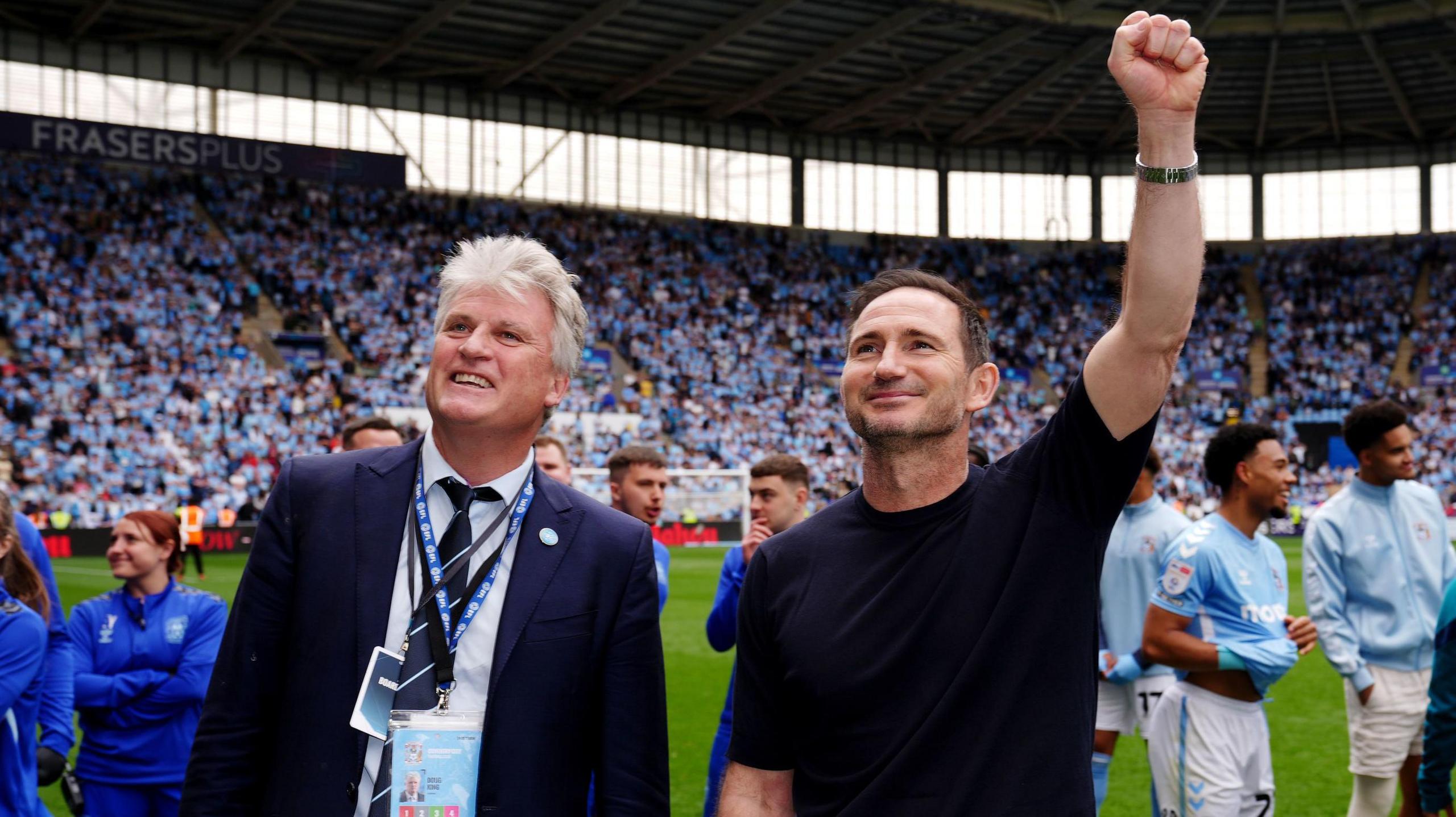 Coventry City owner Doug King pictured with manager Frank Lampard at the Coventry Building Society Arena celebrating with fans. They are both smiling and Frank Lampard has his left first raised in celebration.