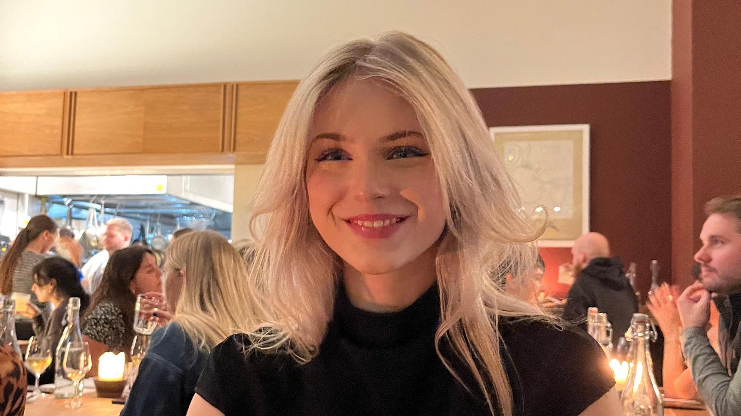 Evie Summers, who has blonde hair, smiling in a restaurant, wearing a black top