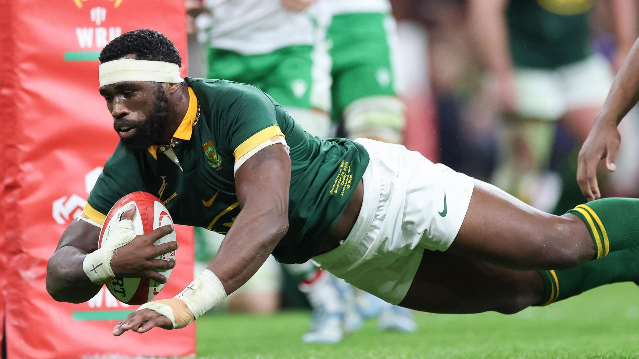 South Africa captain Siya Kolisi with ball under his arm dives over the line to score a try next to a WRU branded post