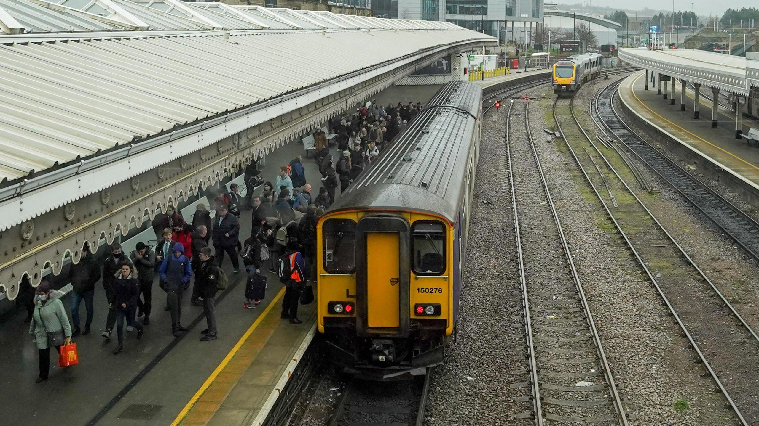 Passengers mill around on a train station platform, where a train has pulled up.