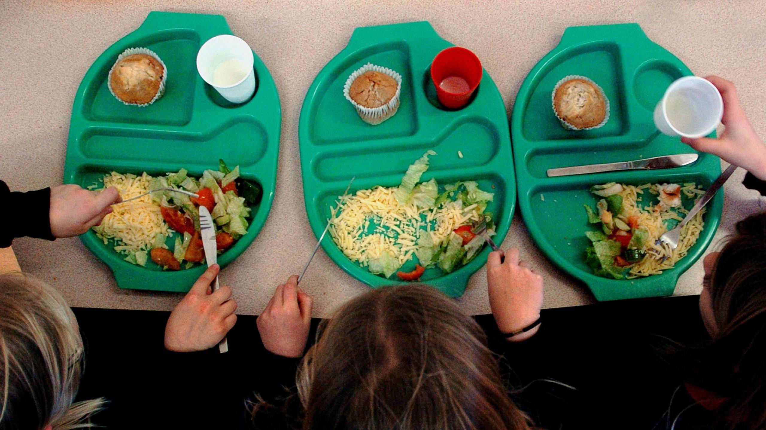 Three children eating salads from three plastic plates