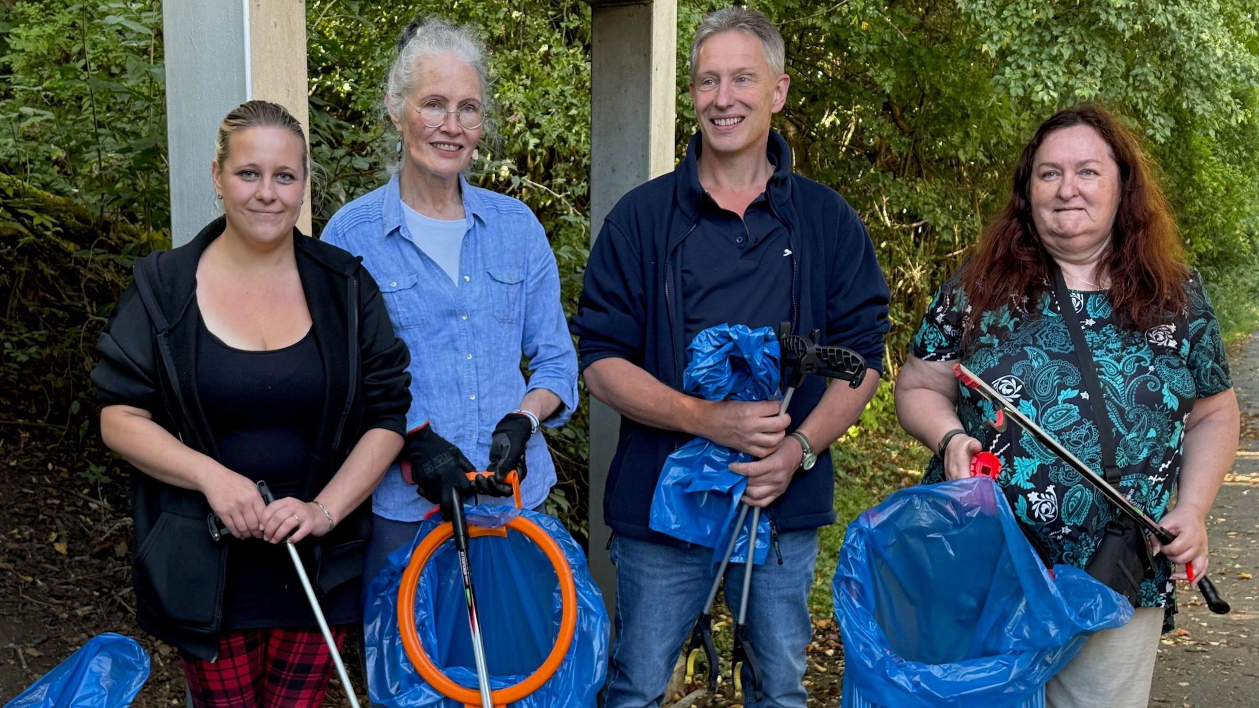 A group of women and a man holding litter-picking equipment