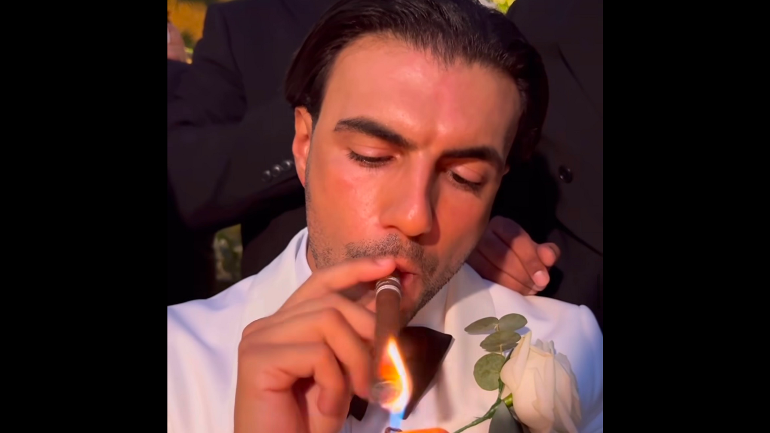 A close up of Ramadan smoking a cigar in his white wedding suit