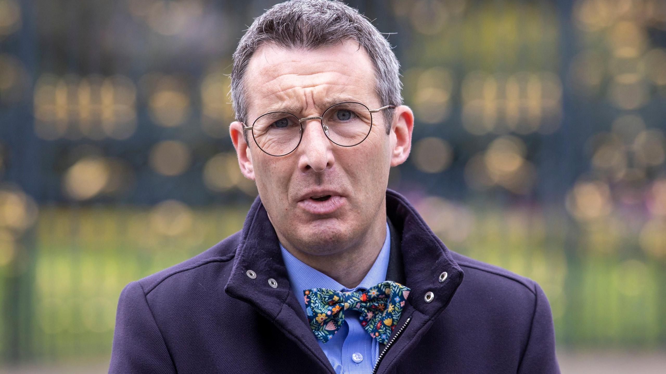 Andrew Muir standing outside. He is wearing a blue jacket, blue shirt and patterned bow tie. He has glasses and grey hair.