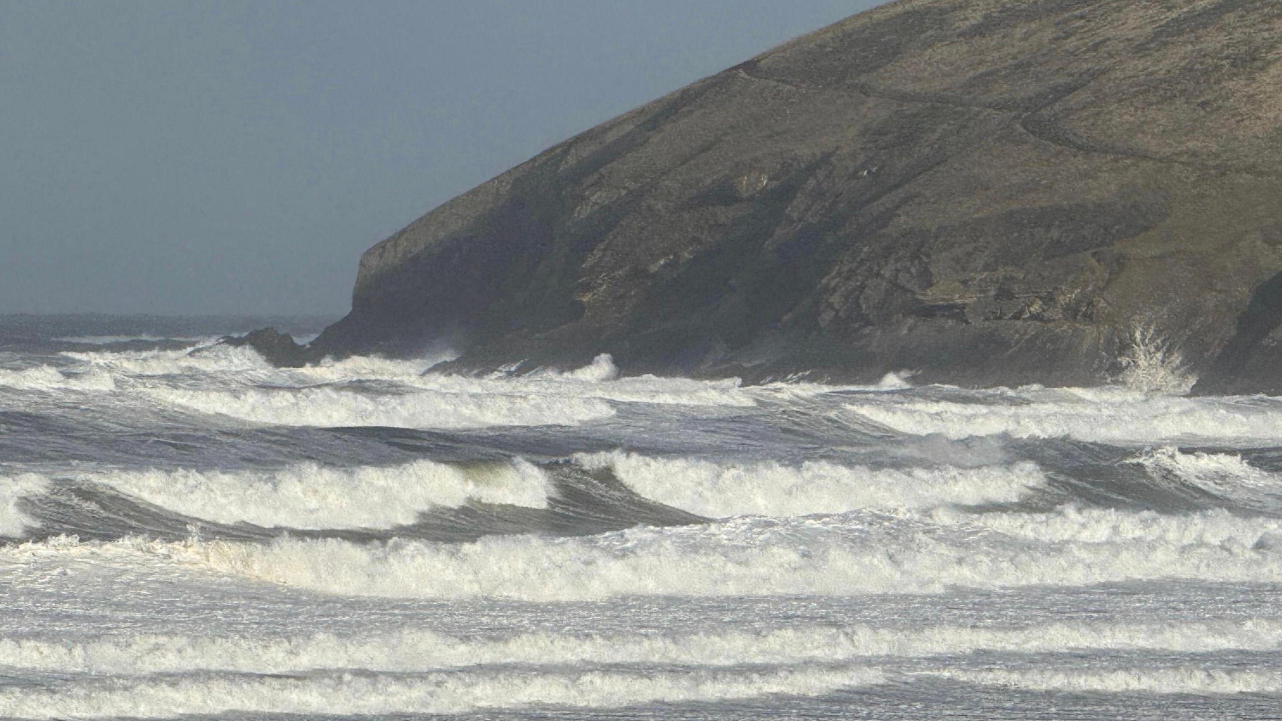 A picture of the sea at Croyde Bay. There are a number of waves, with the hilly coastline visible in the distance.