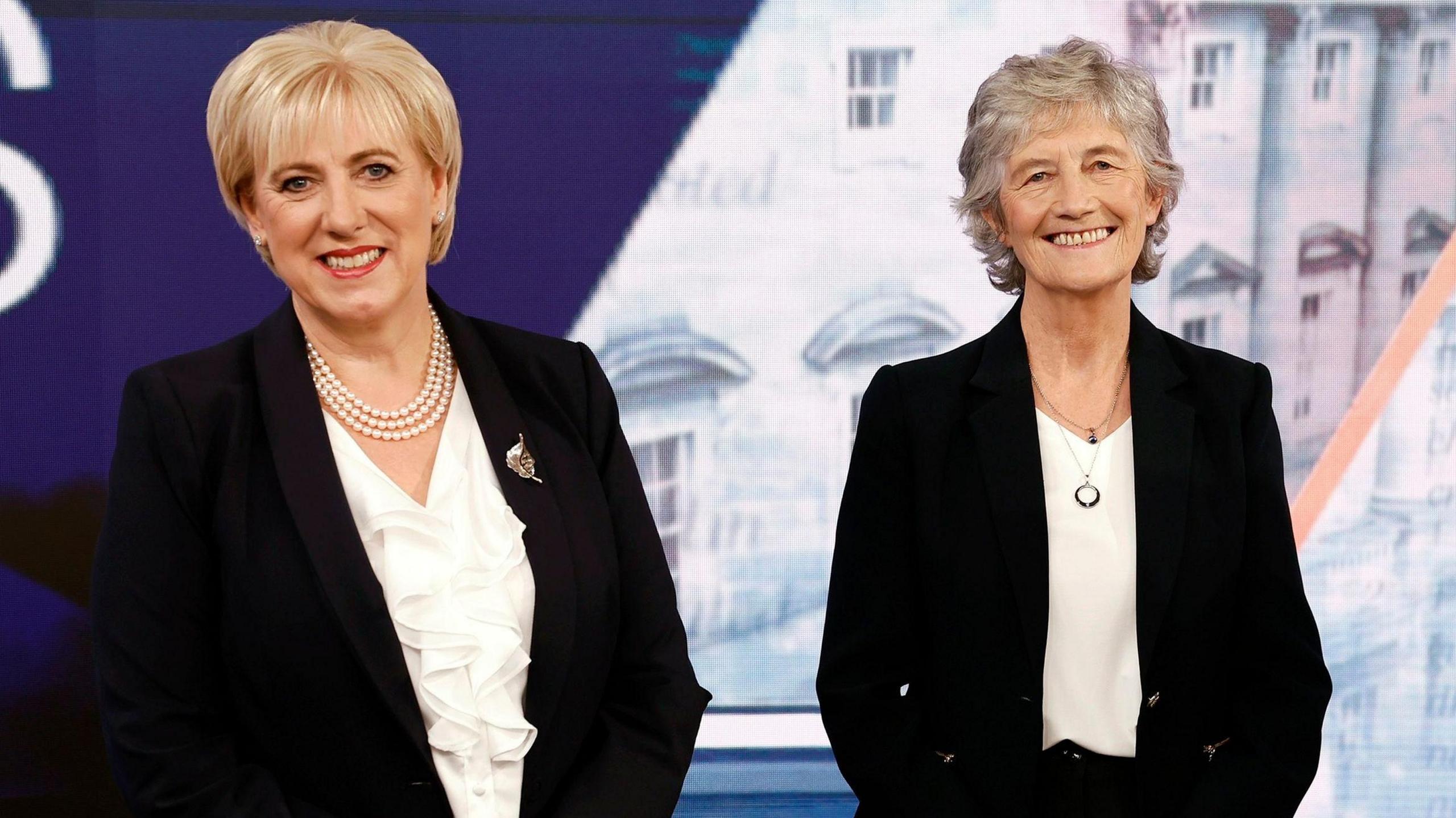 Heather Humphreys has bobbed blonde hair, she is wearing a black jacket and a white blouse. Catherine Connolly has short grey hair. She is also wearing a black jacket and a white blouse.