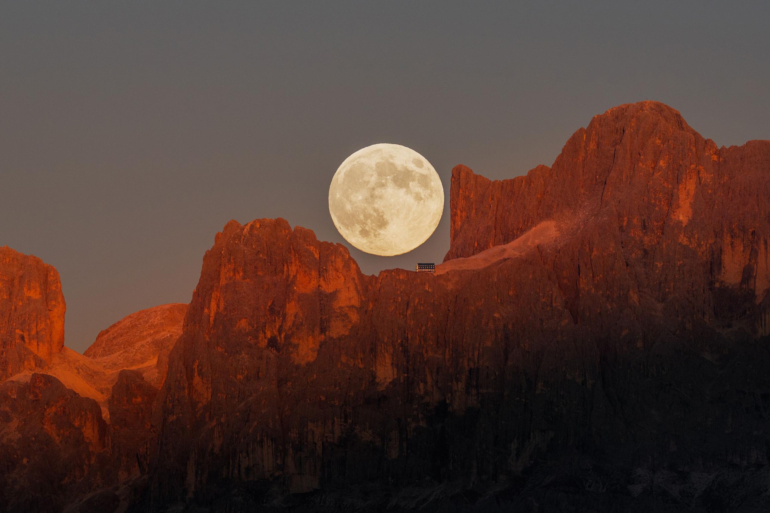 The full Moon rising above the rugged peaks of the Dolomites.