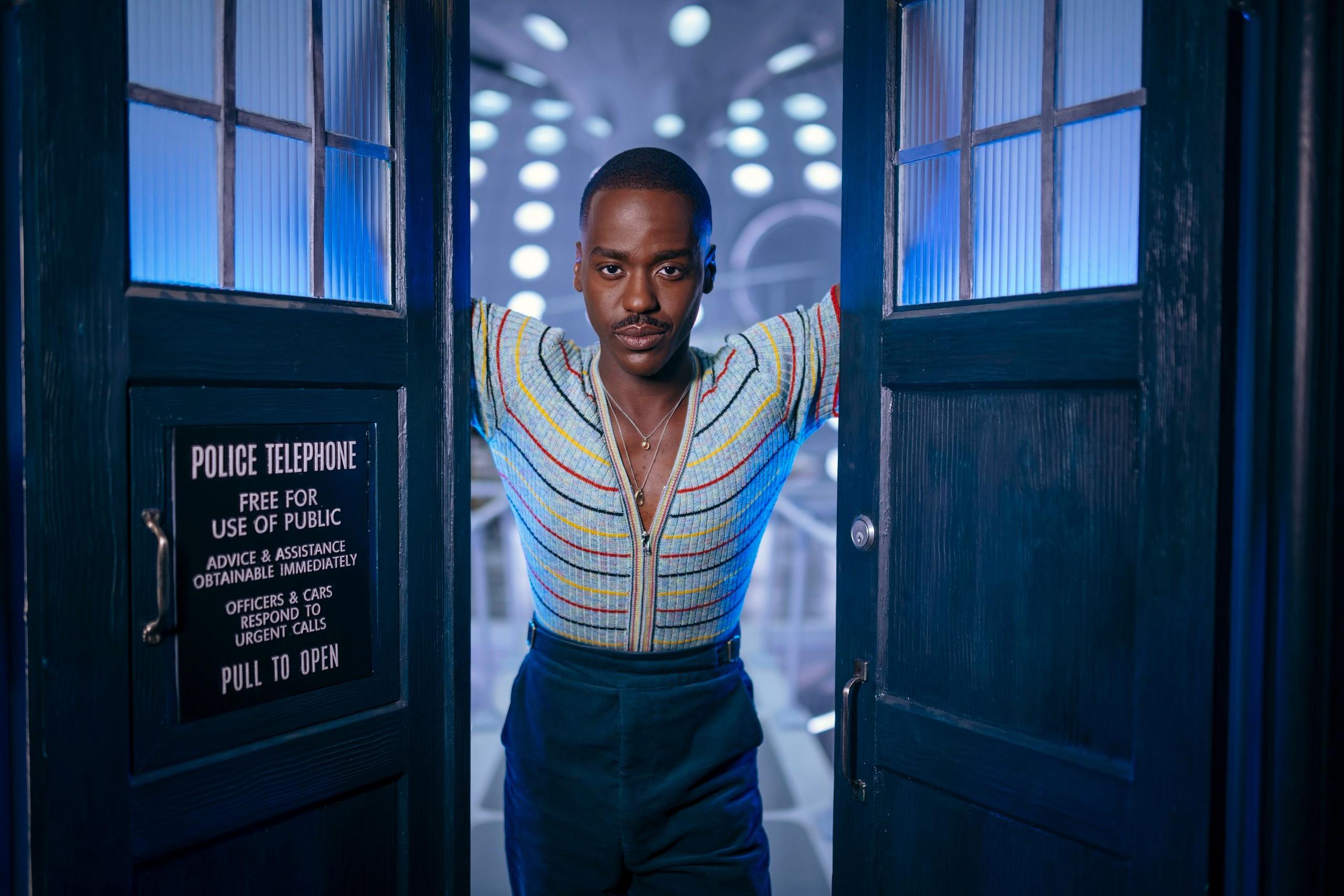 Ncuti Gatwa as The Doctor, looking at the camera while standing in the the doorway of the TARDIS