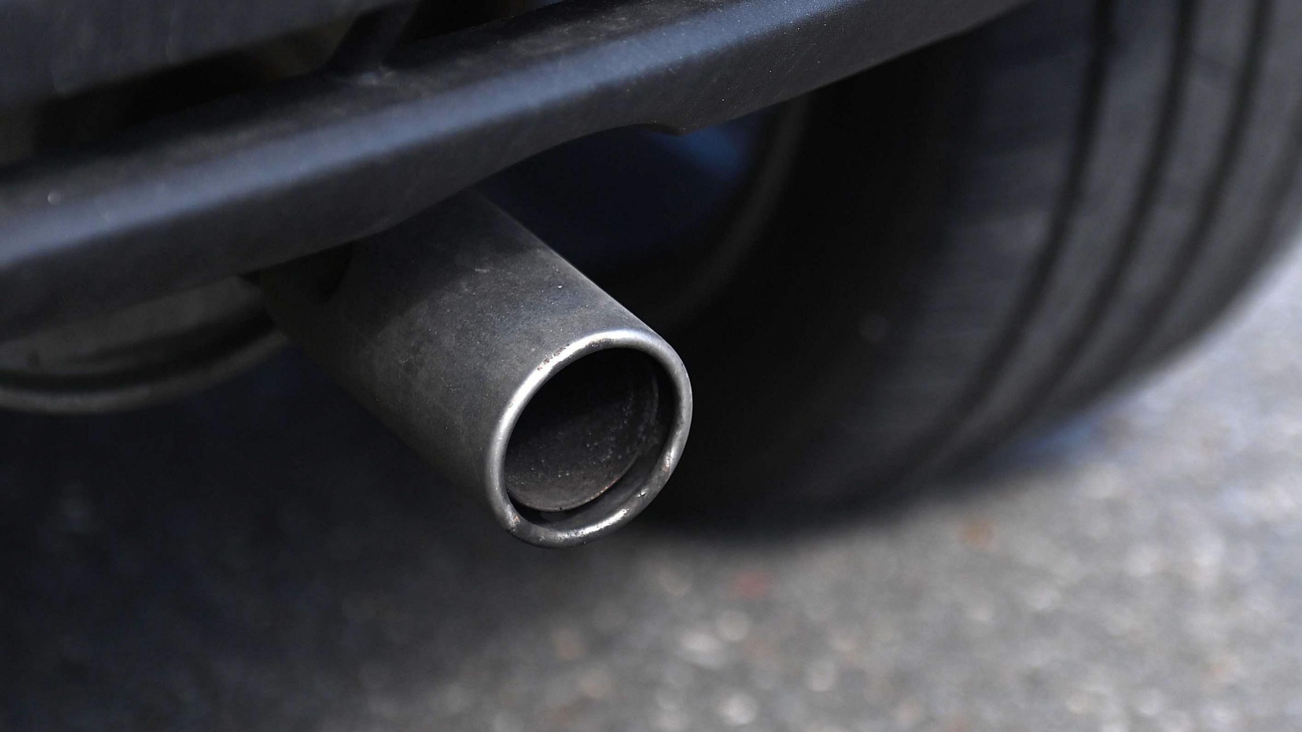 File image showing a close-up of a metal car exhaust pipe, with tarmac visible in the background