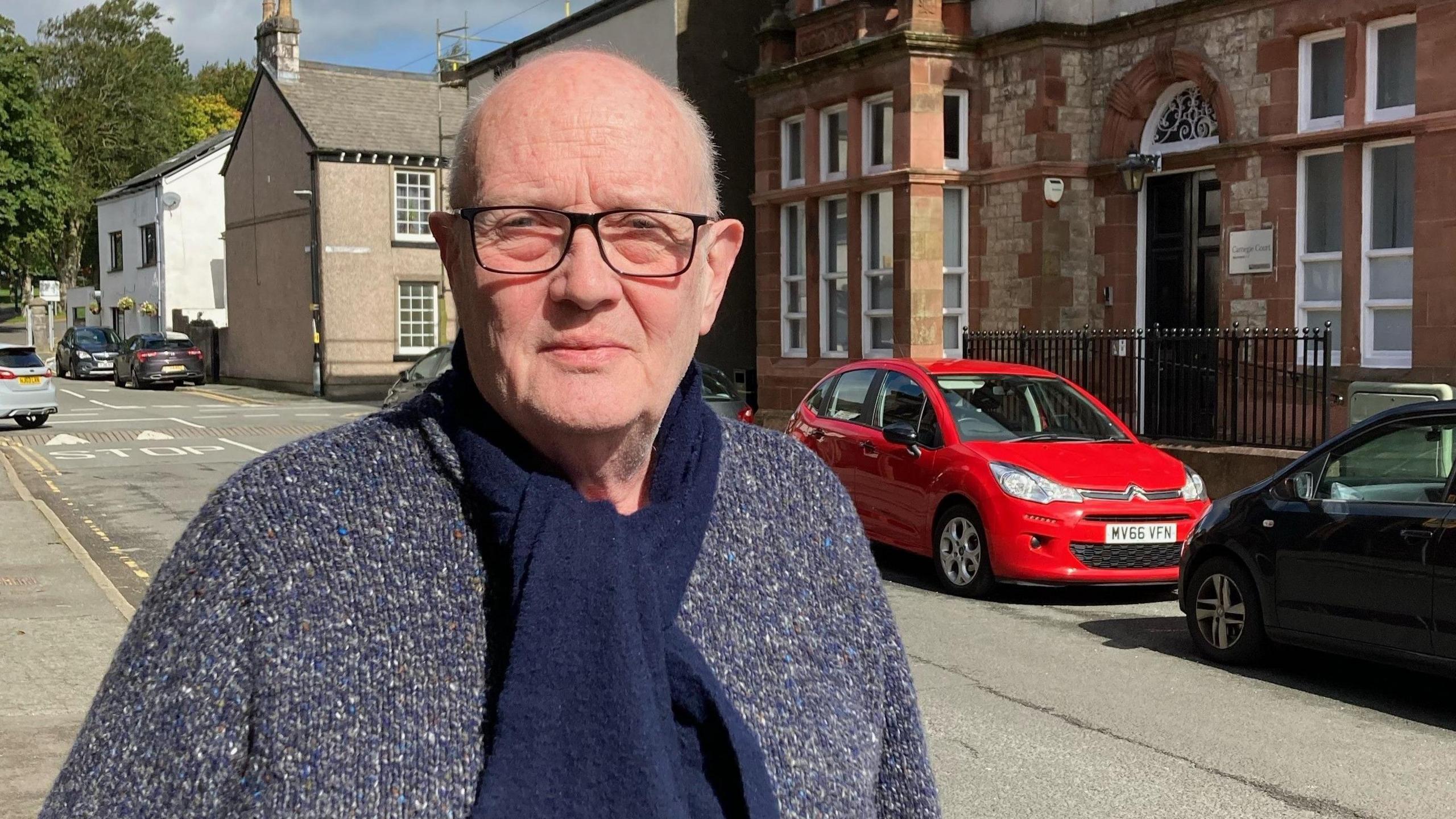 A bald man wearing a woolly jumper looking disappointed