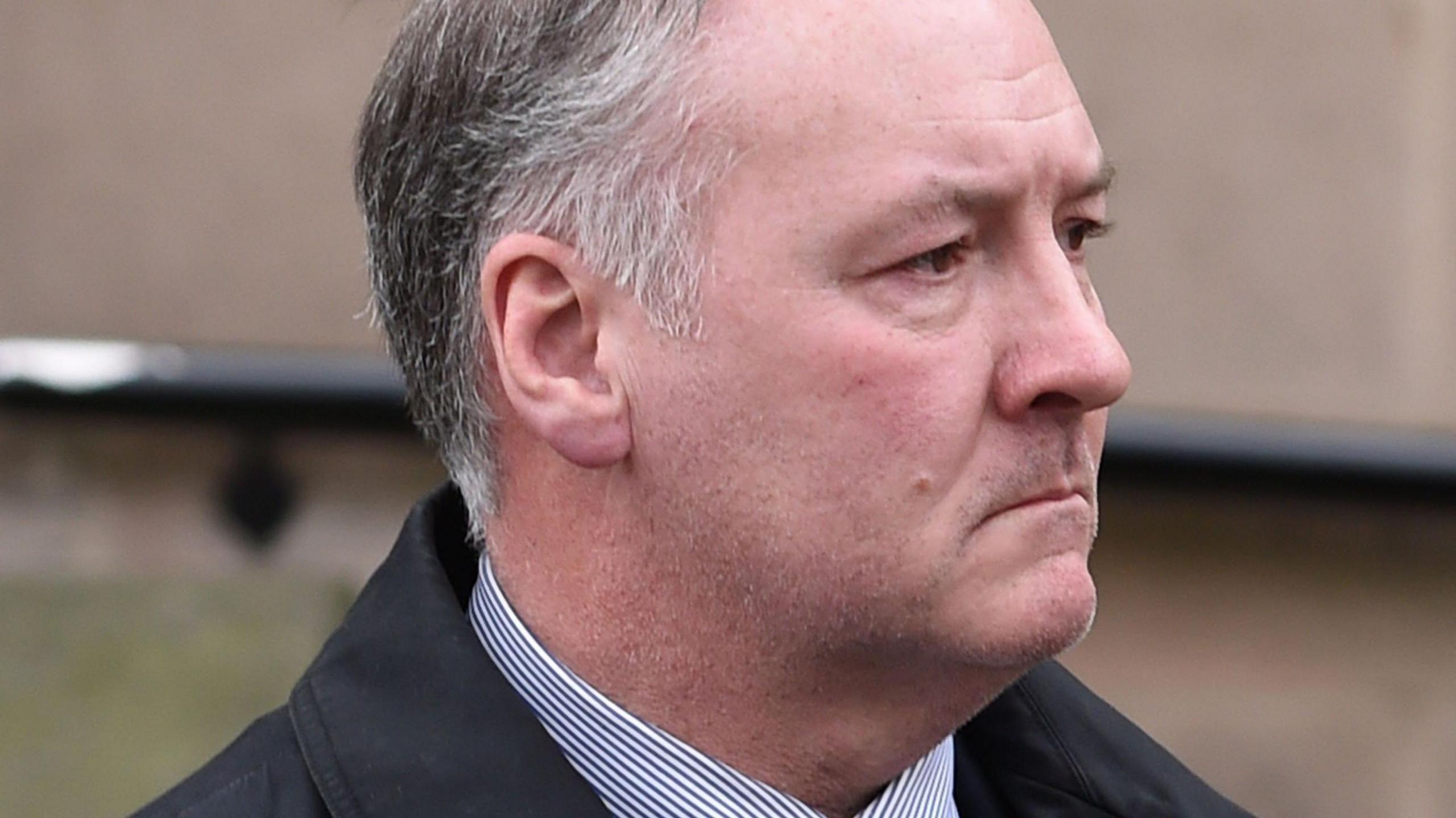 A profile close-up of Ian Paterson, who has short, grey hair and is wearing a striped shirt and a black jacket.