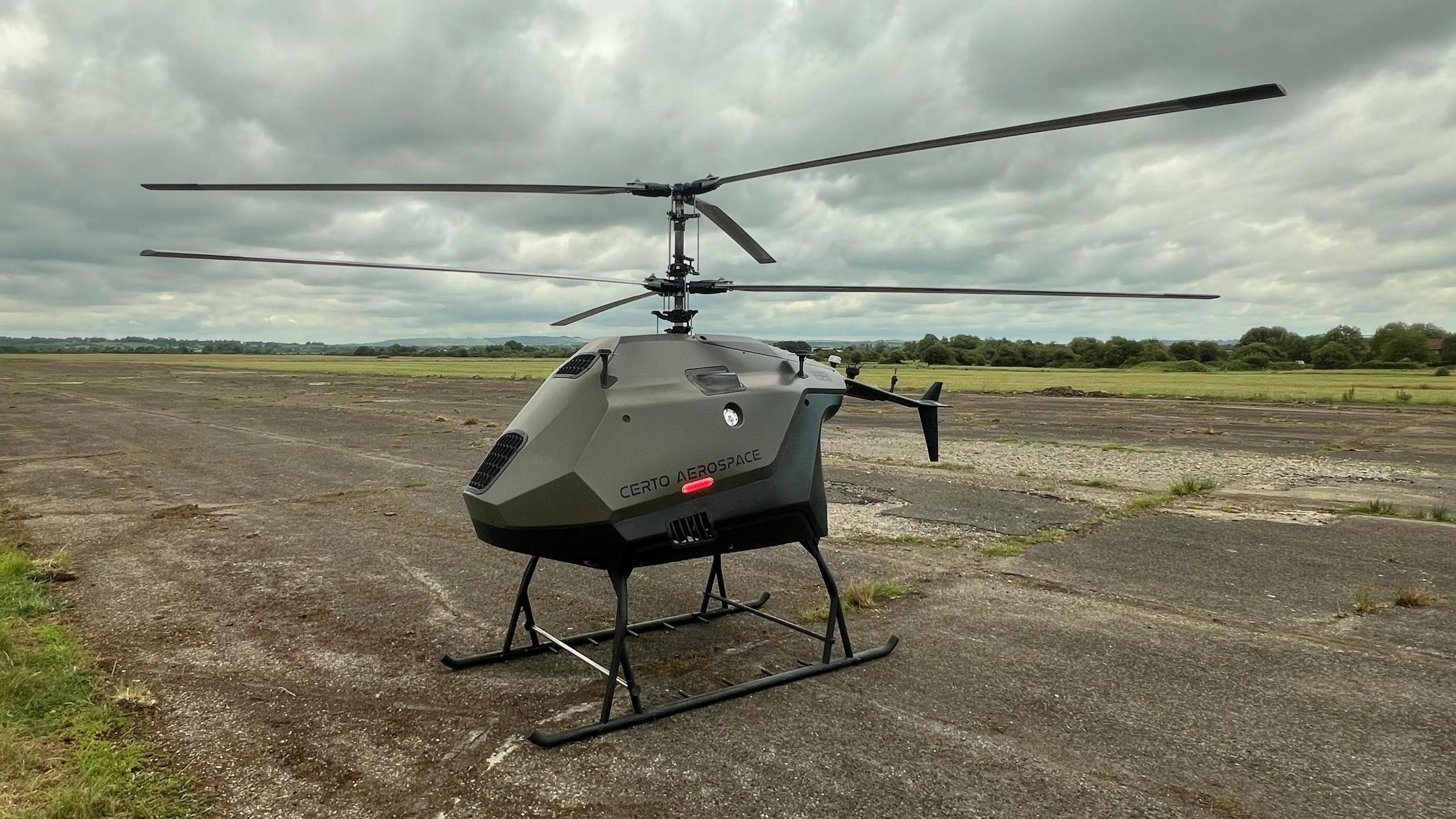 A small green unmanned helicopter on an otherwise empty airfield.