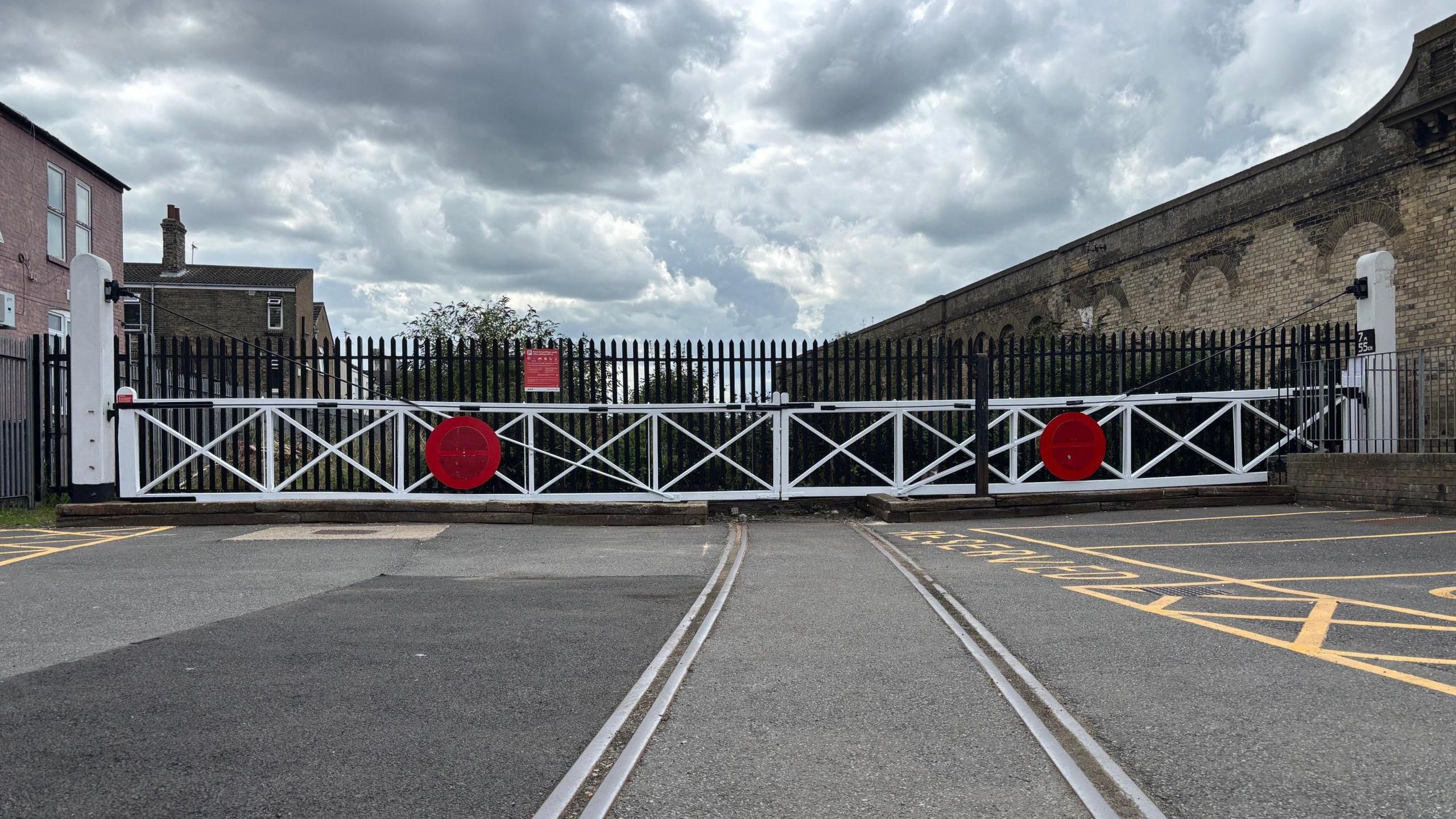 A landscape shot of the white and red gates, in what is now a short stay car park.