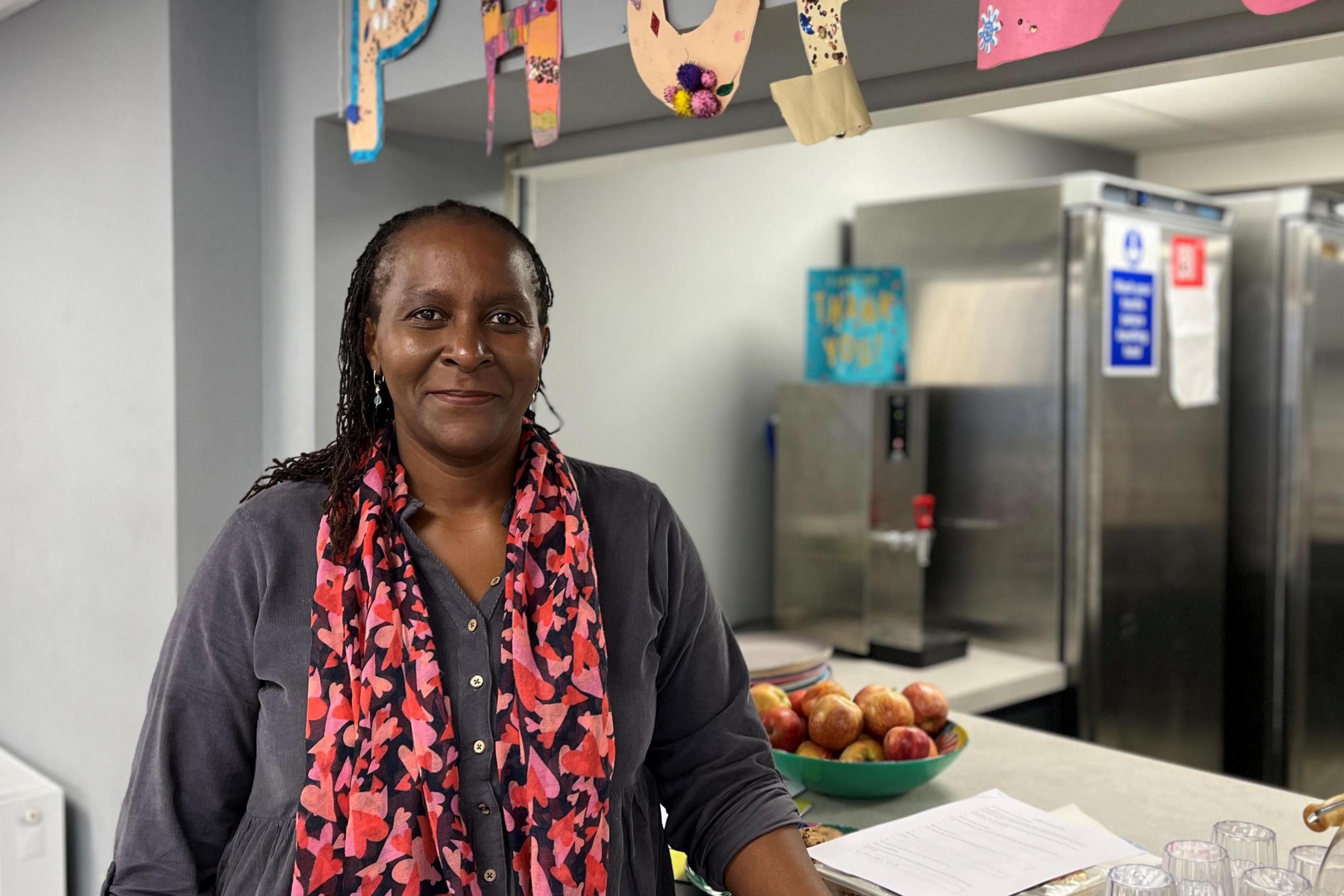 A woman with a bright pink scarf stands in front a community centre kitchen