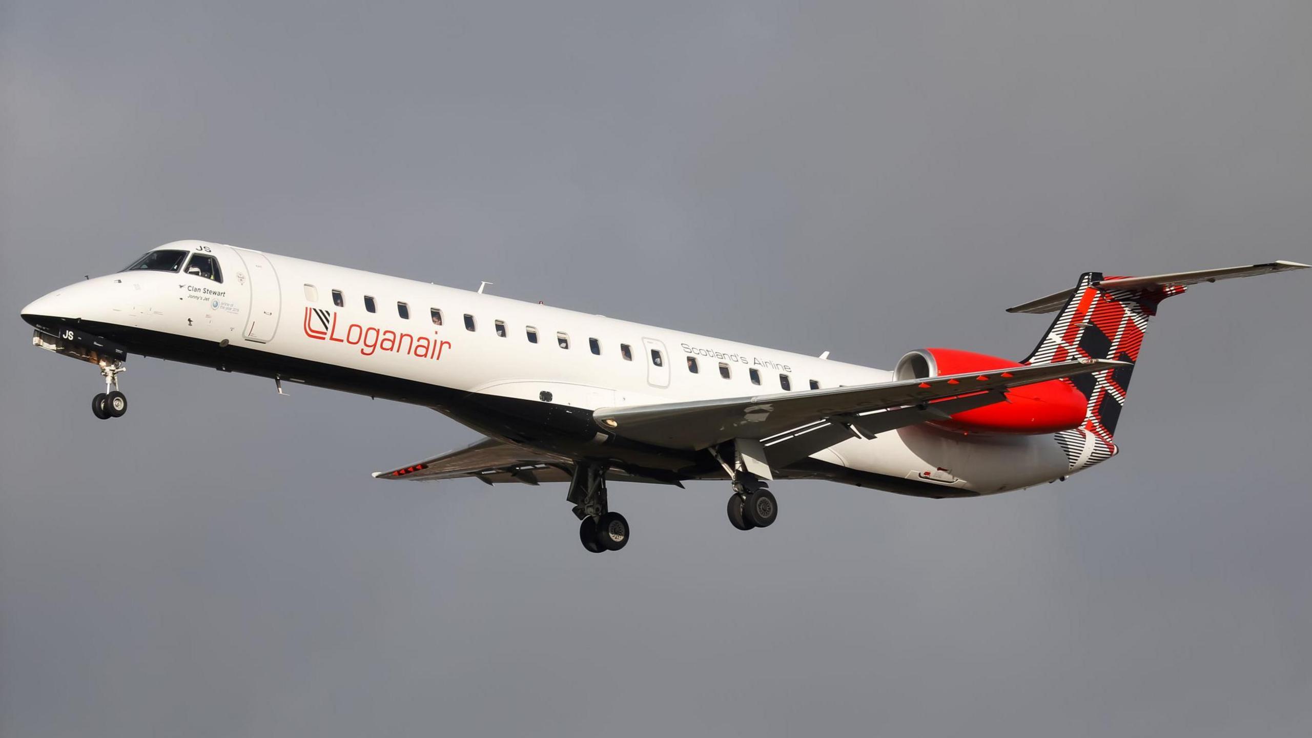 A Loganair passenger jet. The aircraft has a white fuselage, red jet engines and a tail decorated with a red, black and white tartan. The jet has its wheels down as it comes into land.