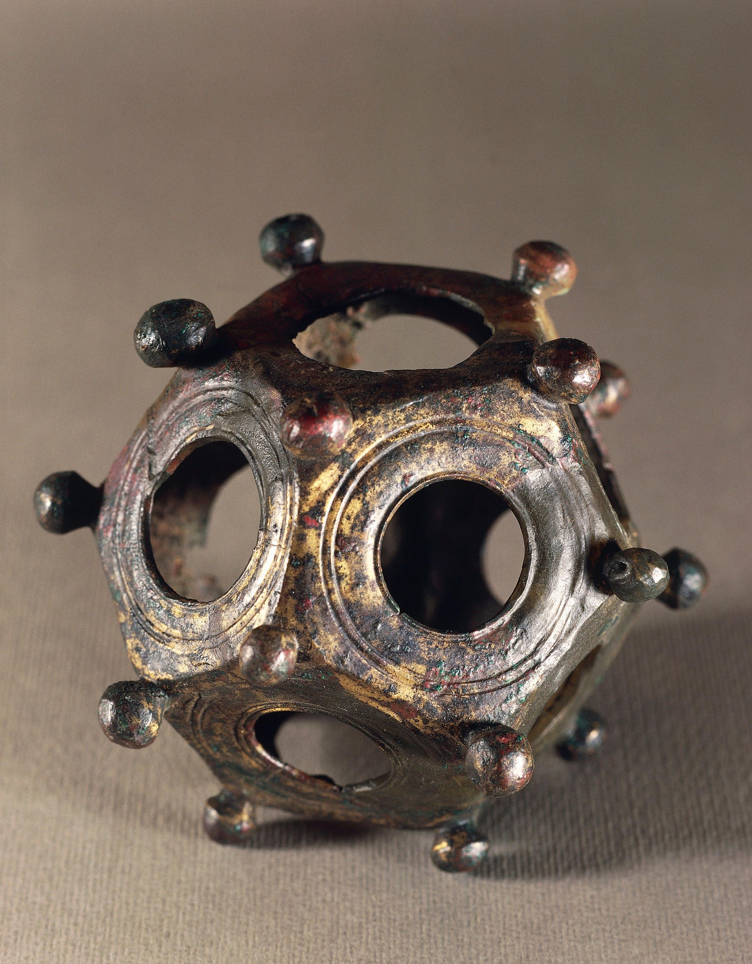 a portrait image of a dodecahedron made of bronze with holes on each side and small balls of the same material postioned on each corner