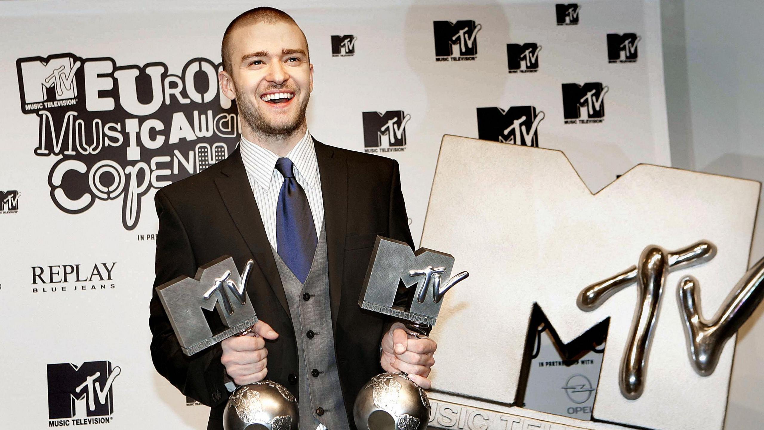Justin Timberlake smiling and holding two MTV Europe Music Awards alongside a giant MTV logo at the MTV Europe Music Awards 2006 in Copenhagen