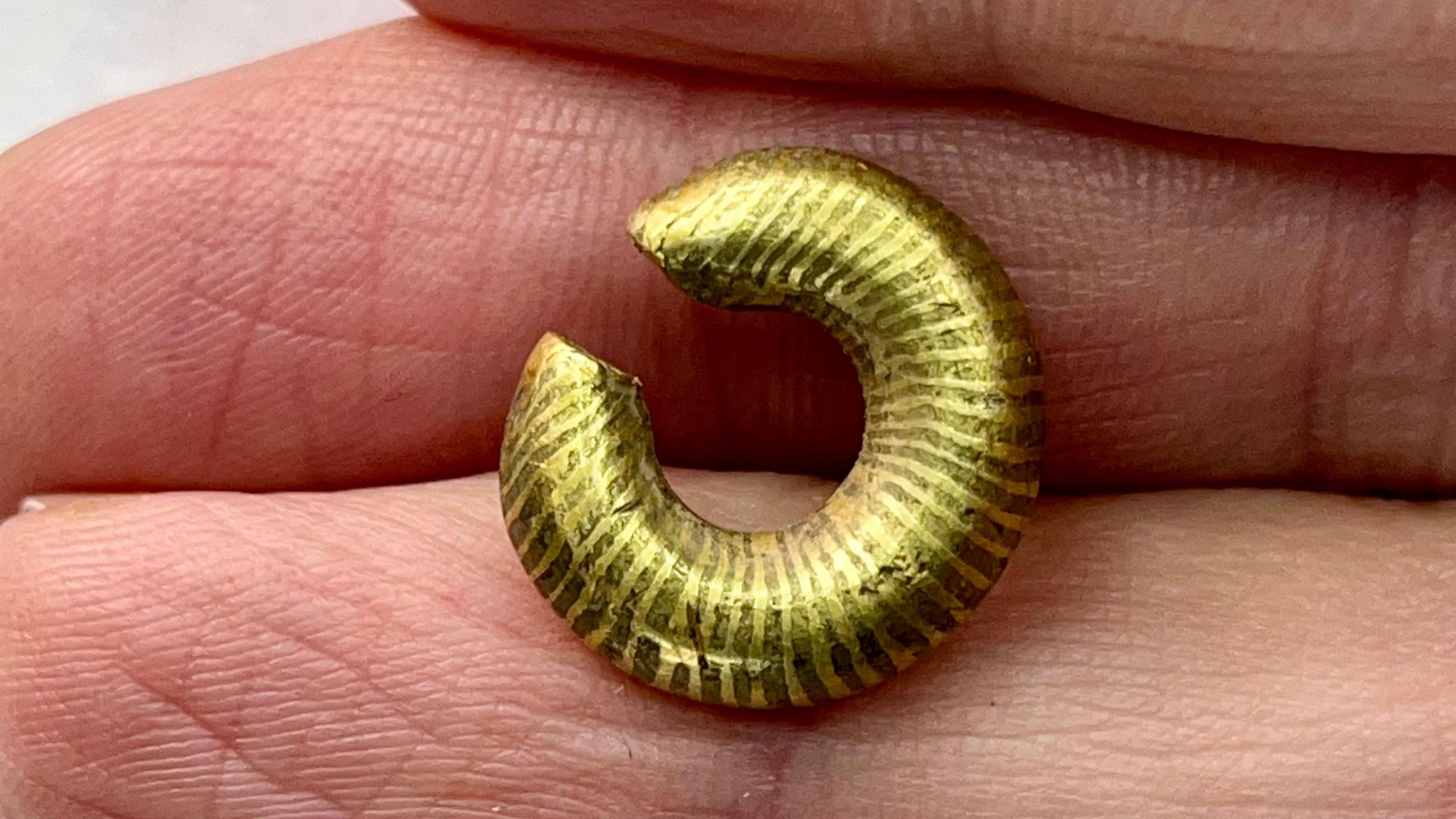 A small gold ring resting between someone's fingers. It had a gap in it about a third of the diameter of the inside of the ring and light and dark banding roughly coming from the centre.